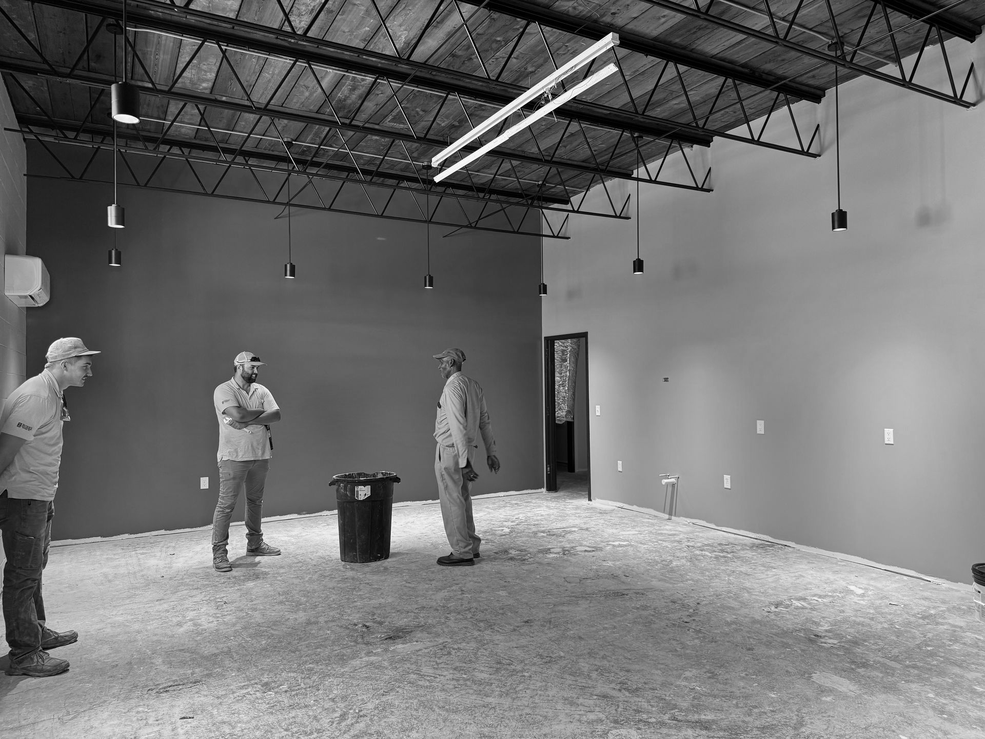 Three men in a construction site with exposed ceiling, grey walls, and dirt floor.