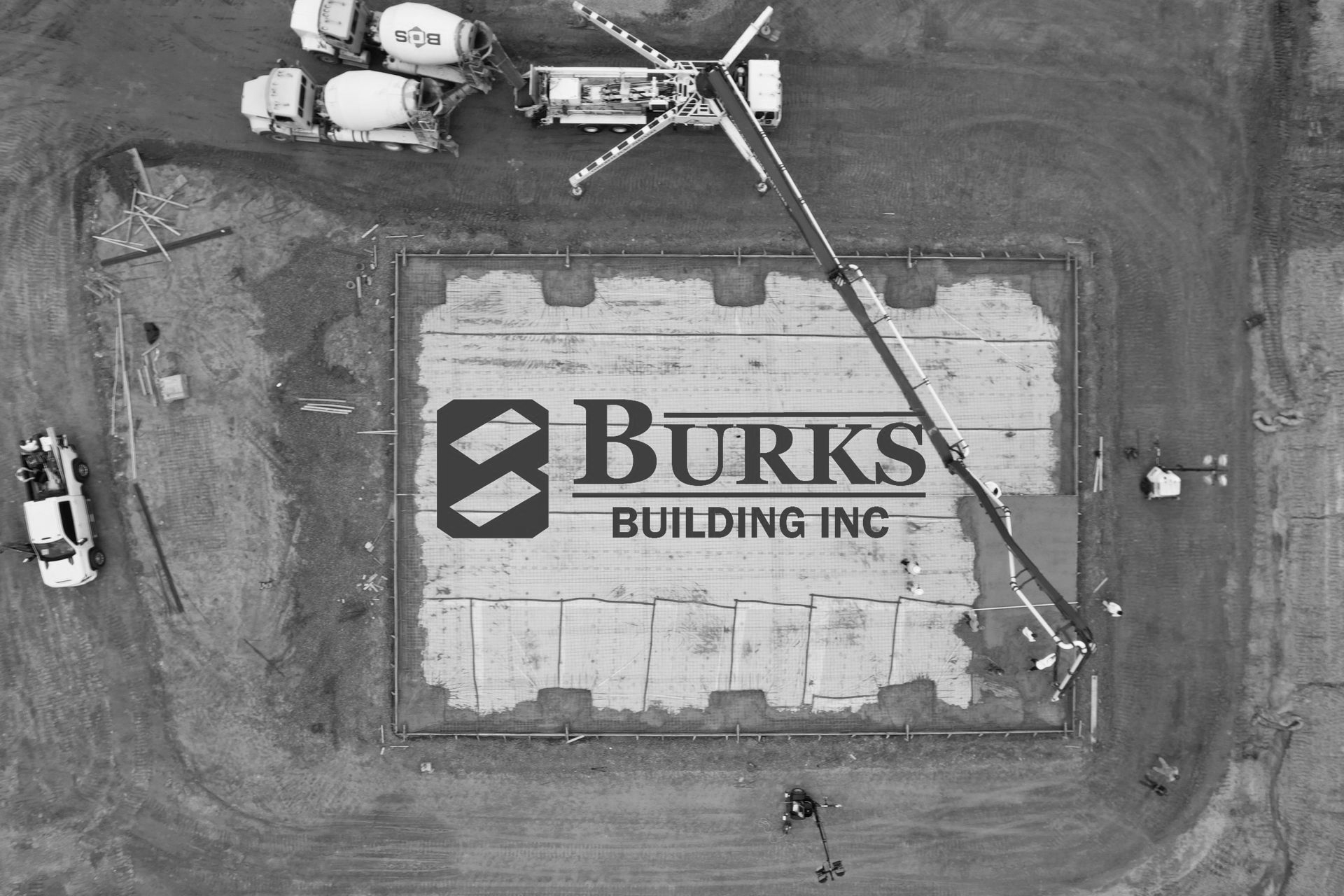 Aerial view of construction site; Burks Building Inc. logo on concrete slab, concrete trucks present.