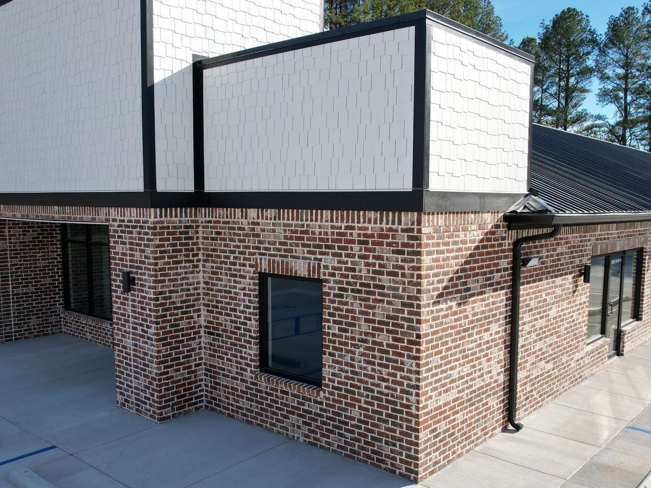 Brick building with white shingle siding, black trim, and windows under a blue sky.