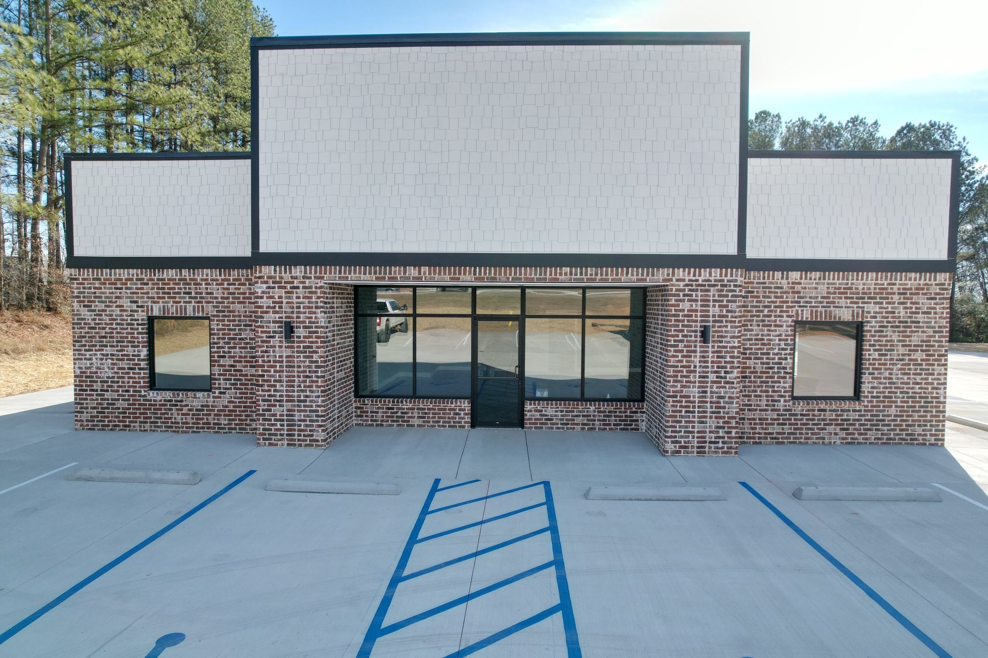 Brick building with white accents, black trim, and blue parking lines. Empty windows and door.