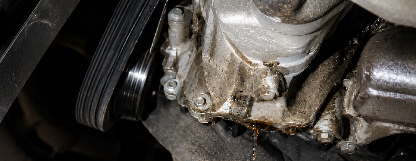 Close-up of a greasy metal engine part with a black pulley and worn belt.