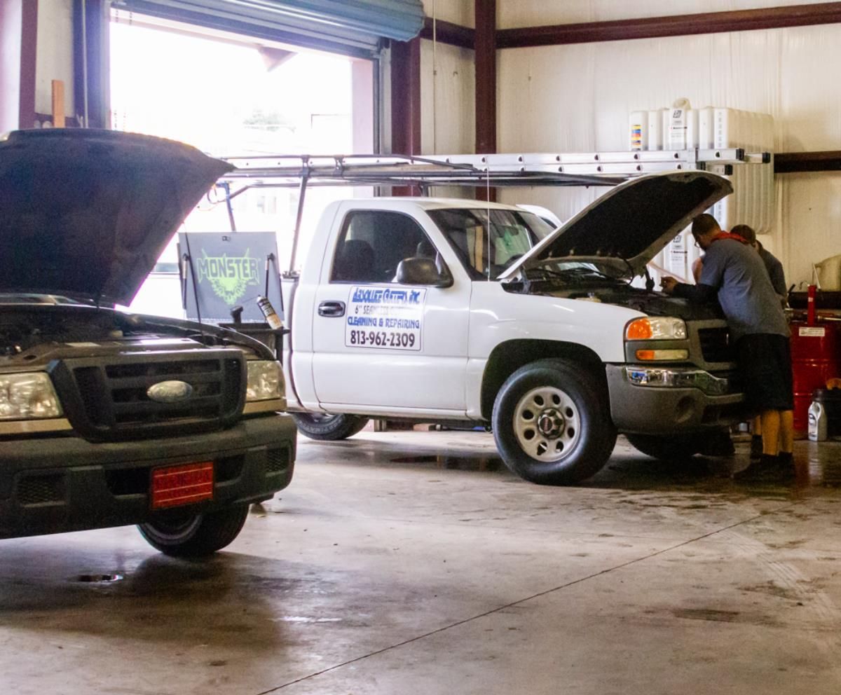 Two trucks are parked in a garage with the hoods open