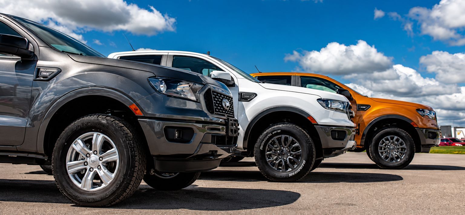 Three parked pickup trucks in black, white, and orange under a blue sky