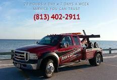 A red tow truck is parked on the side of the road next to the ocean.
