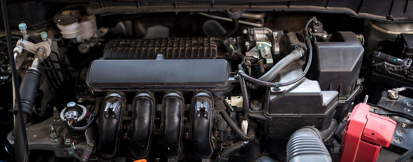 Car engine bay, showing various components like intake manifold, battery, and fluid reservoirs.