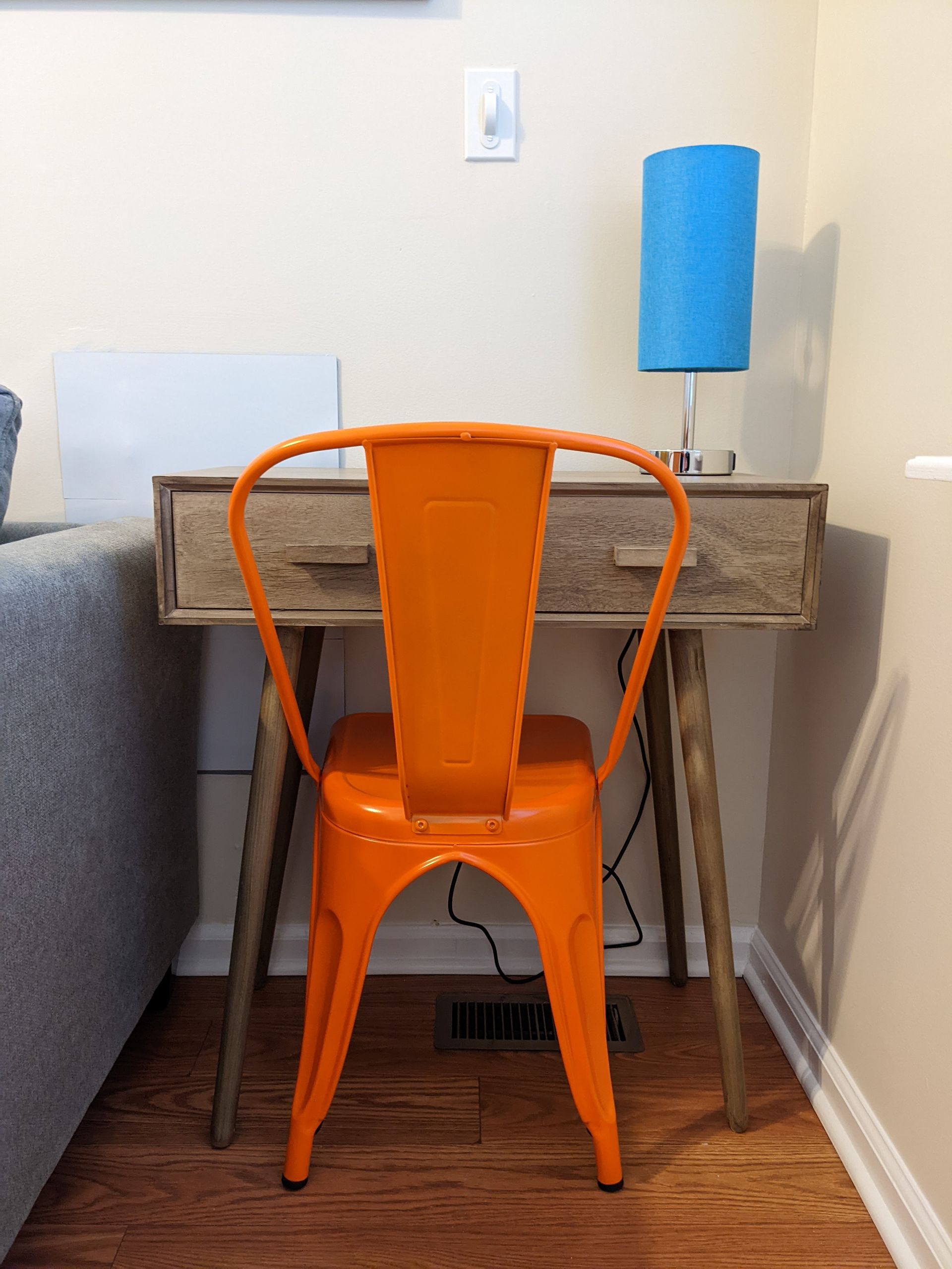 An orange chair sits at a desk next to a lamp