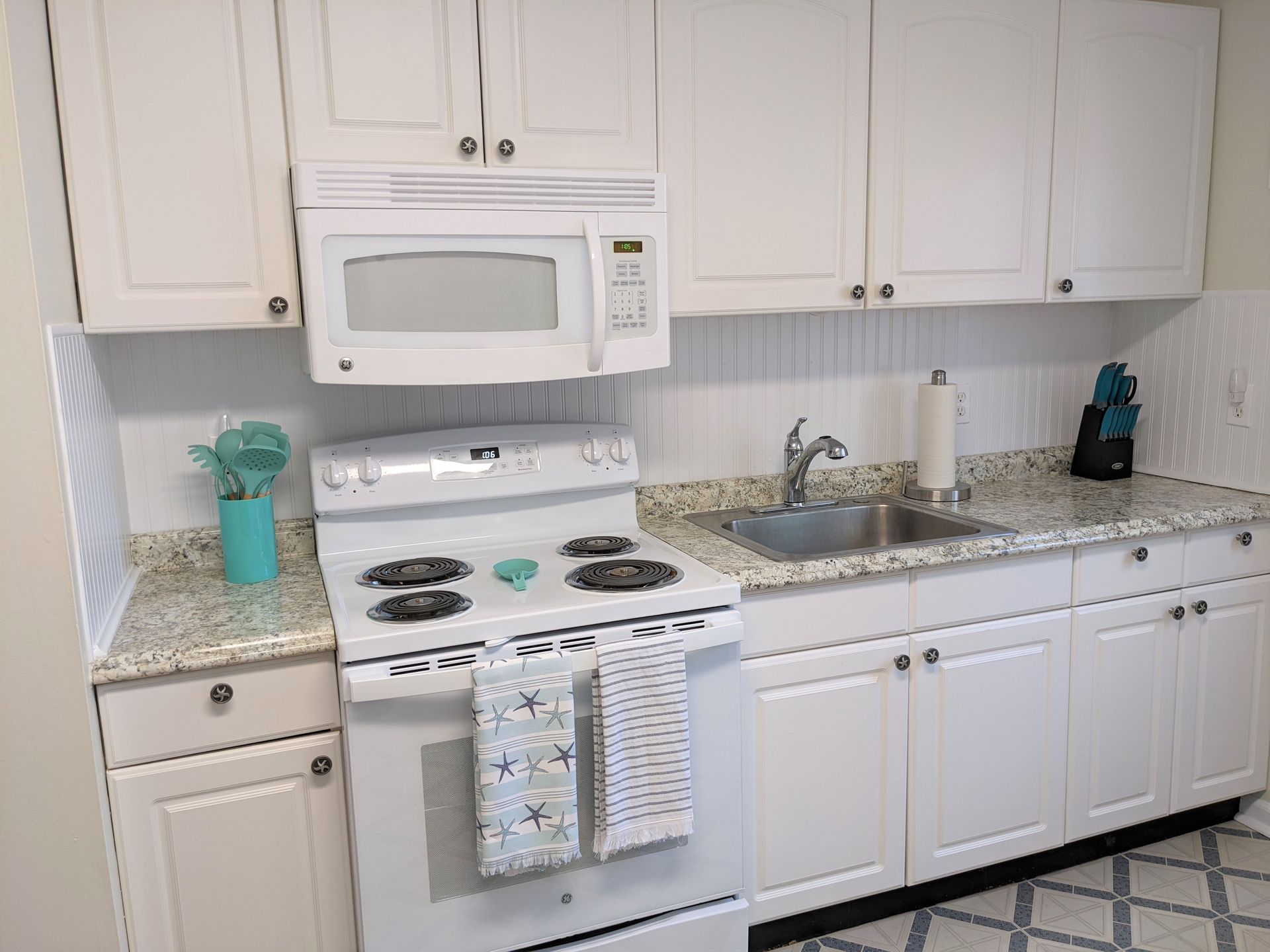 A kitchen with white cabinets , a stove , microwave and sink.