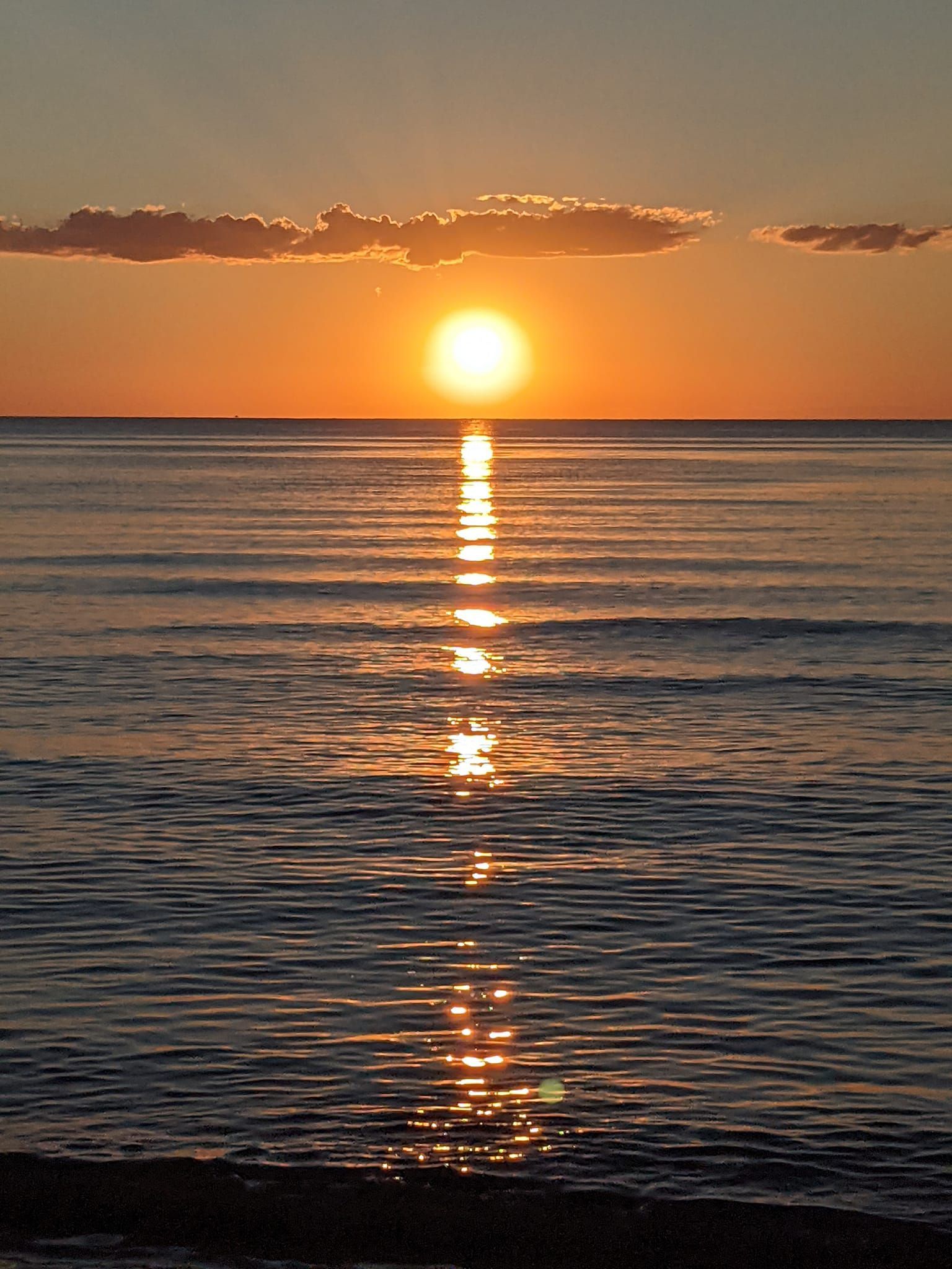 The sun is setting over the ocean and reflected in the water.