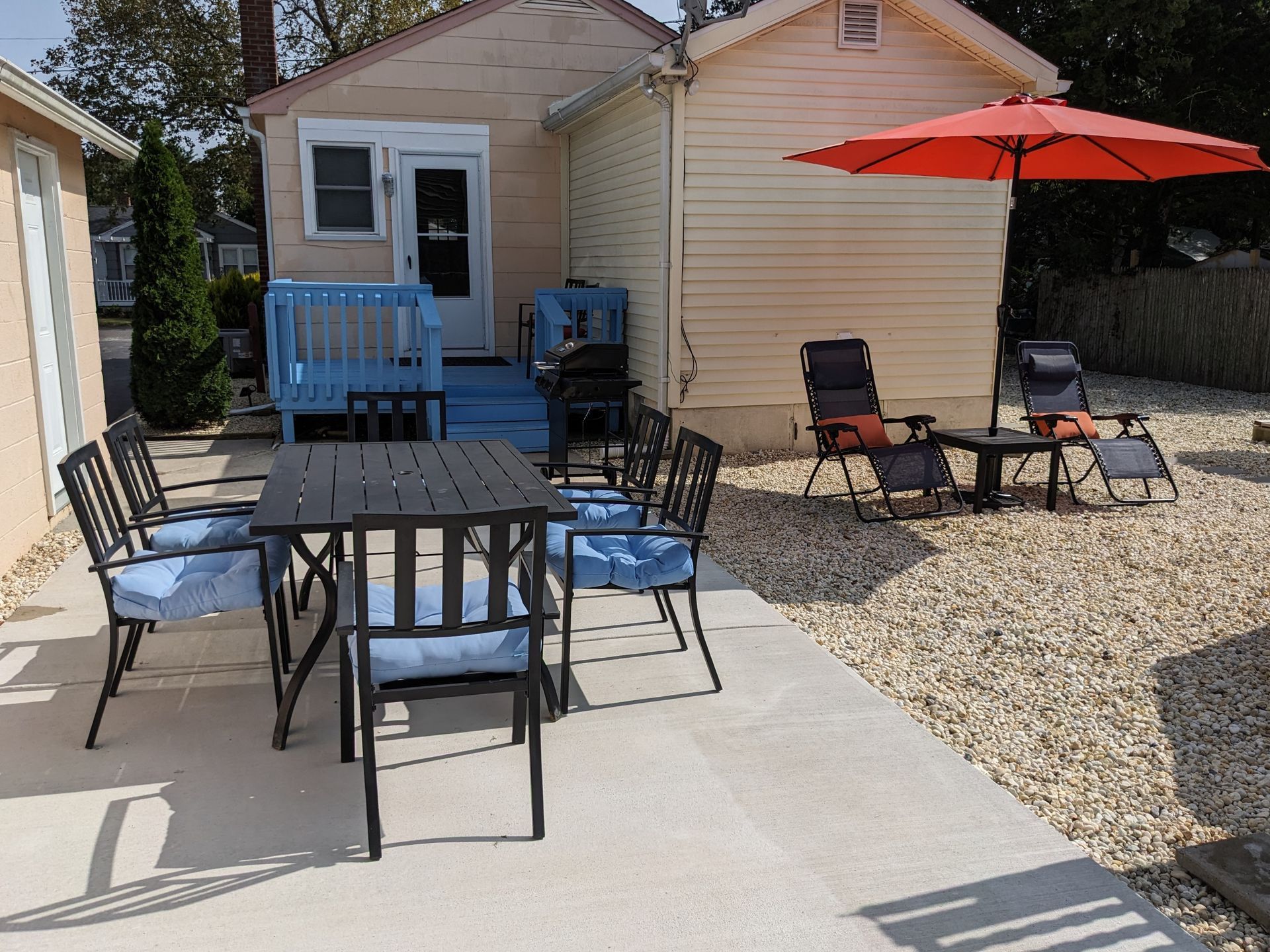 A patio with a table and chairs and an orange umbrella