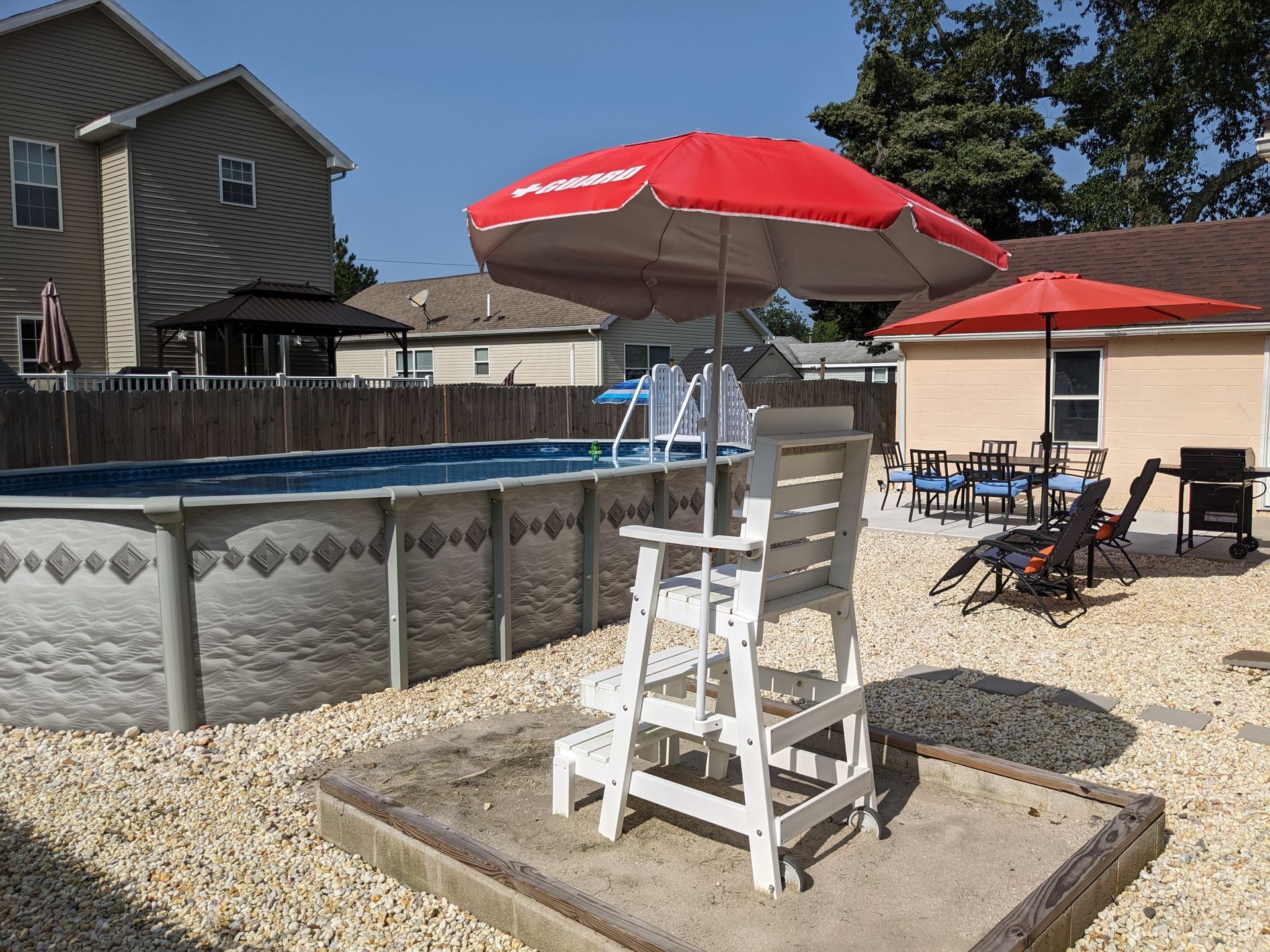 A lifeguard chair with a red umbrella in front of a pool