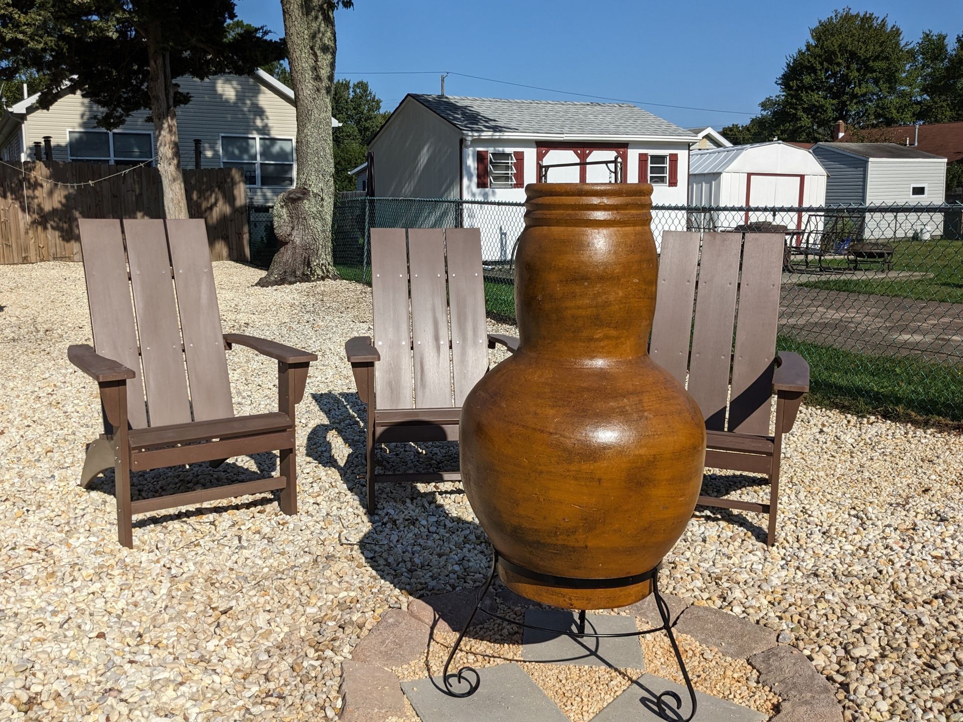 A large vase sits in the middle of a gravel area between two chairs