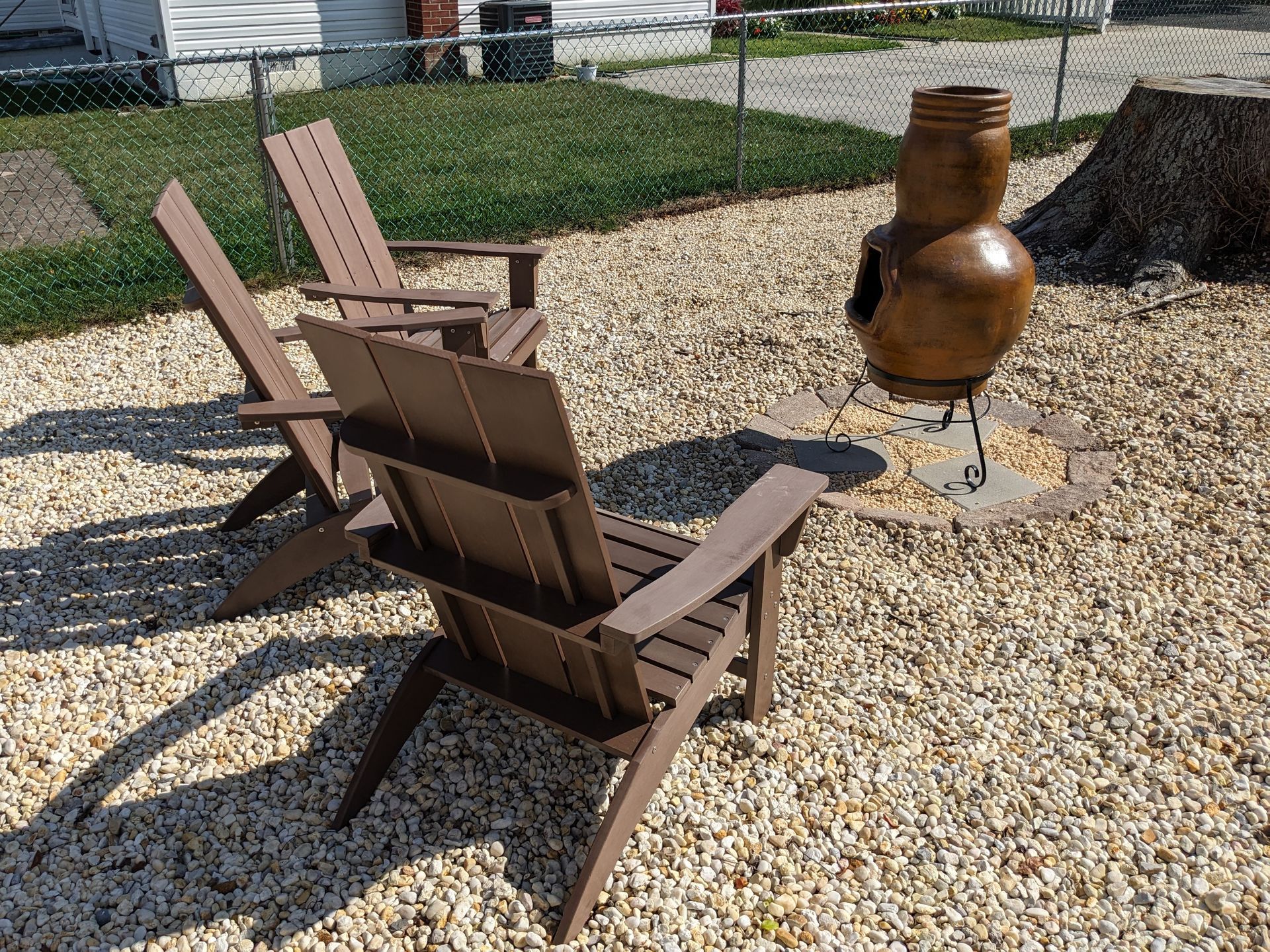 Two wooden chairs are sitting in a gravel area next to a fire pit.