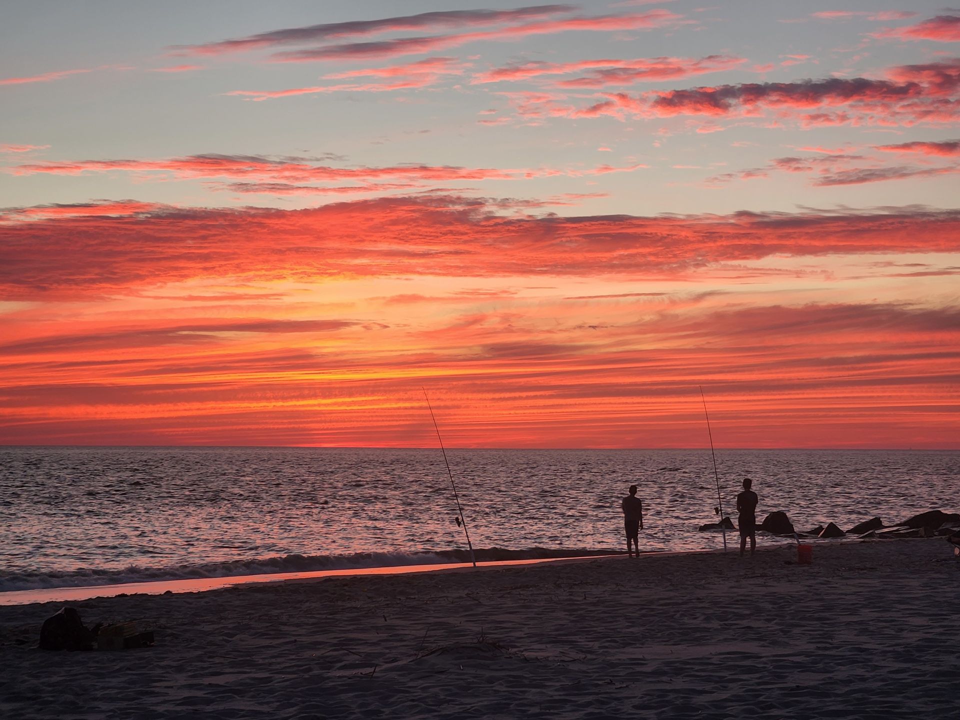 A group of people are fishing on the beach at sunset.