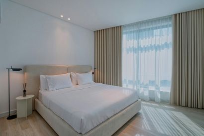 Bedroom with white walls, bed, curtains, and floor, lit by sunlight.