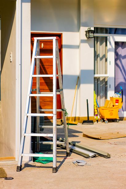 Aluminum ladder propped against a door on a construction site. Other tools and materials visible.