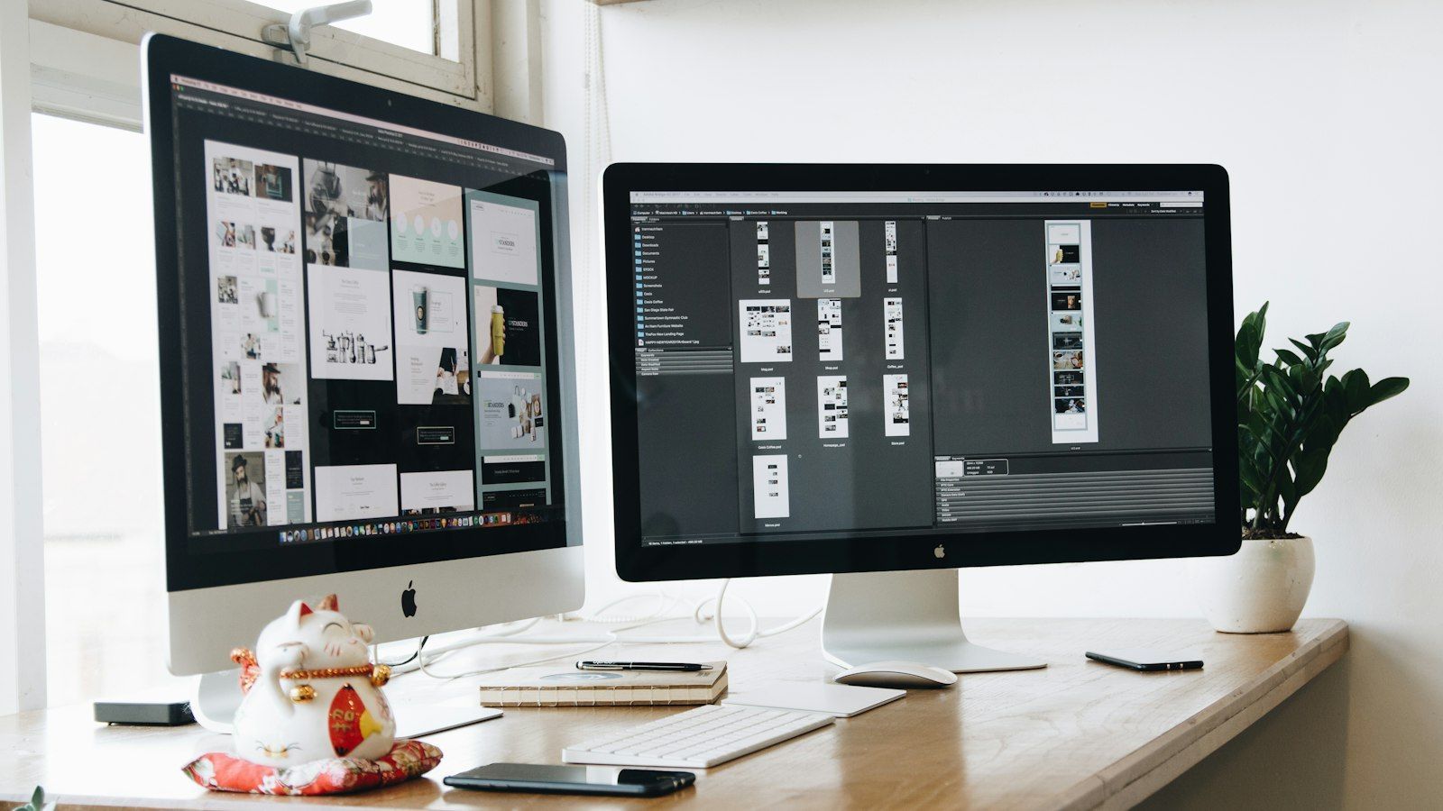 Dual desktop monitors on a bright desk with a keyboard, mouse, and small potted plant in a modern office.