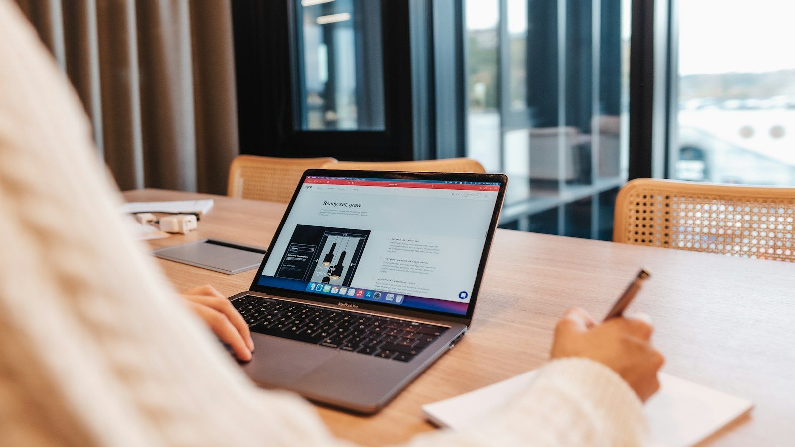 Person working at a laptop in a modern office, with a notebook and pen on the table.