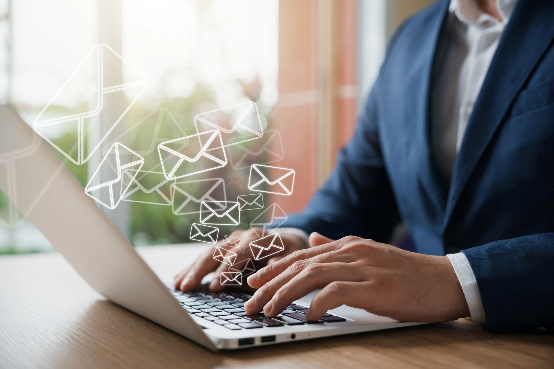 Hands typing on a laptop with email icons floating above, in a bright office setting