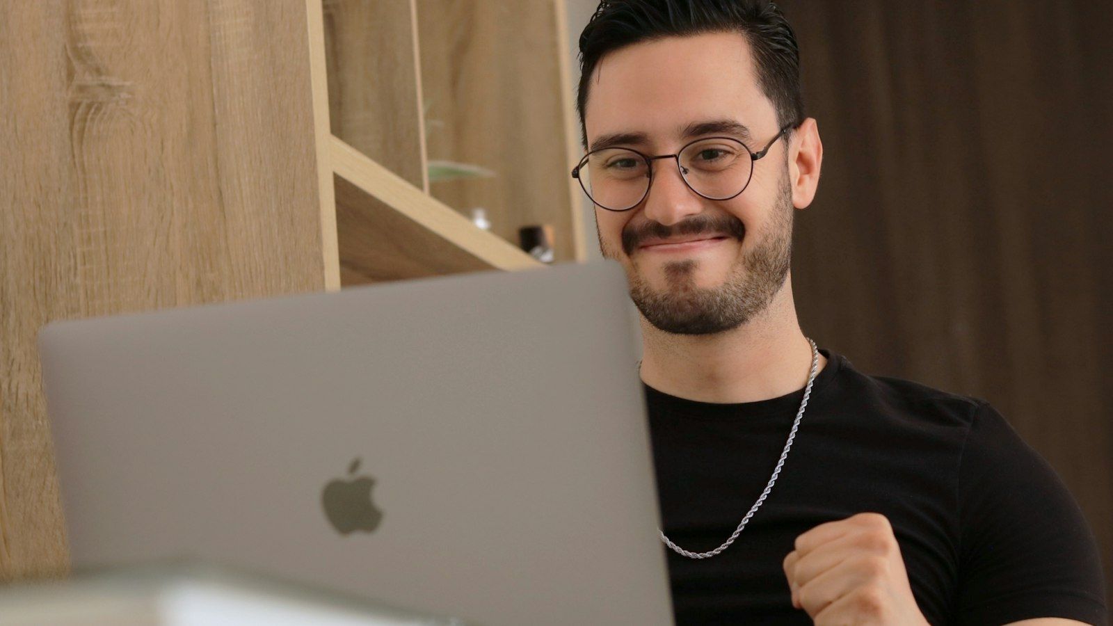 Smiling man with glasses using a laptop in a warm-toned home office
