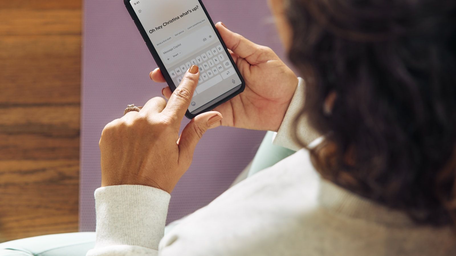 Person using a smartphone while seated on a couch, tapping a screen with text displayed.