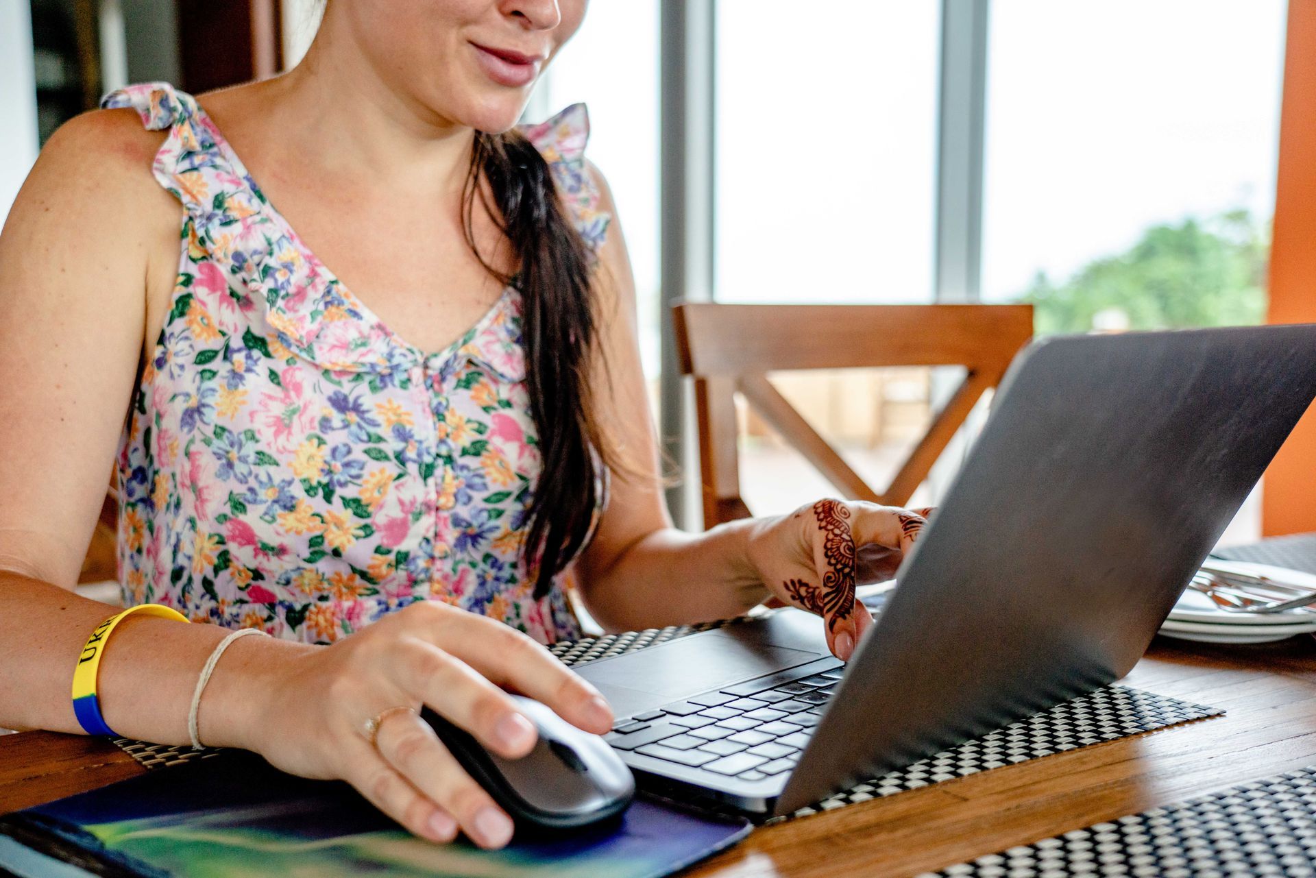 Woman using a laptop and mouse at a wooden table in a bright room