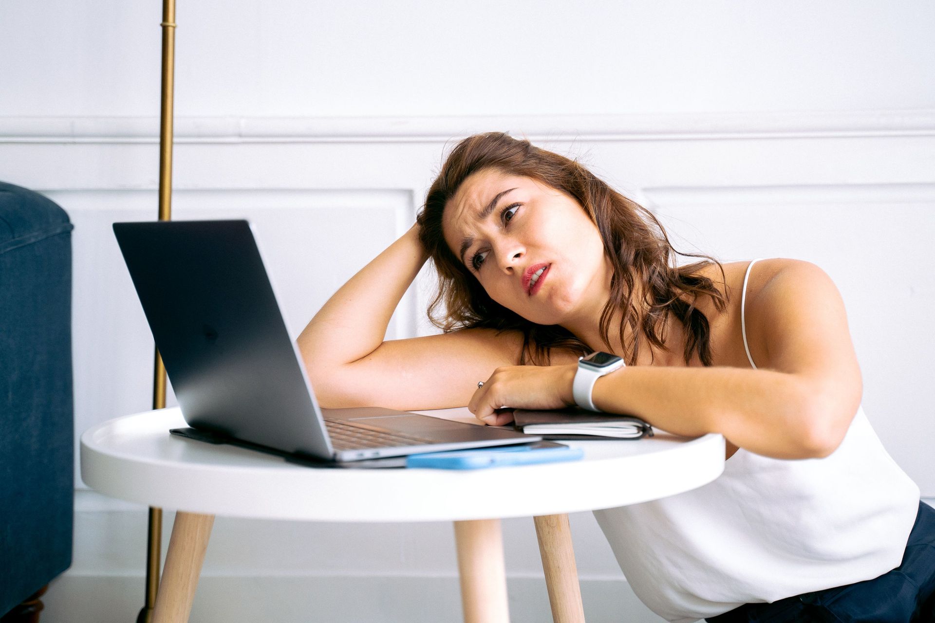 Tired woman resting her head on her hand beside a laptop at a small round table