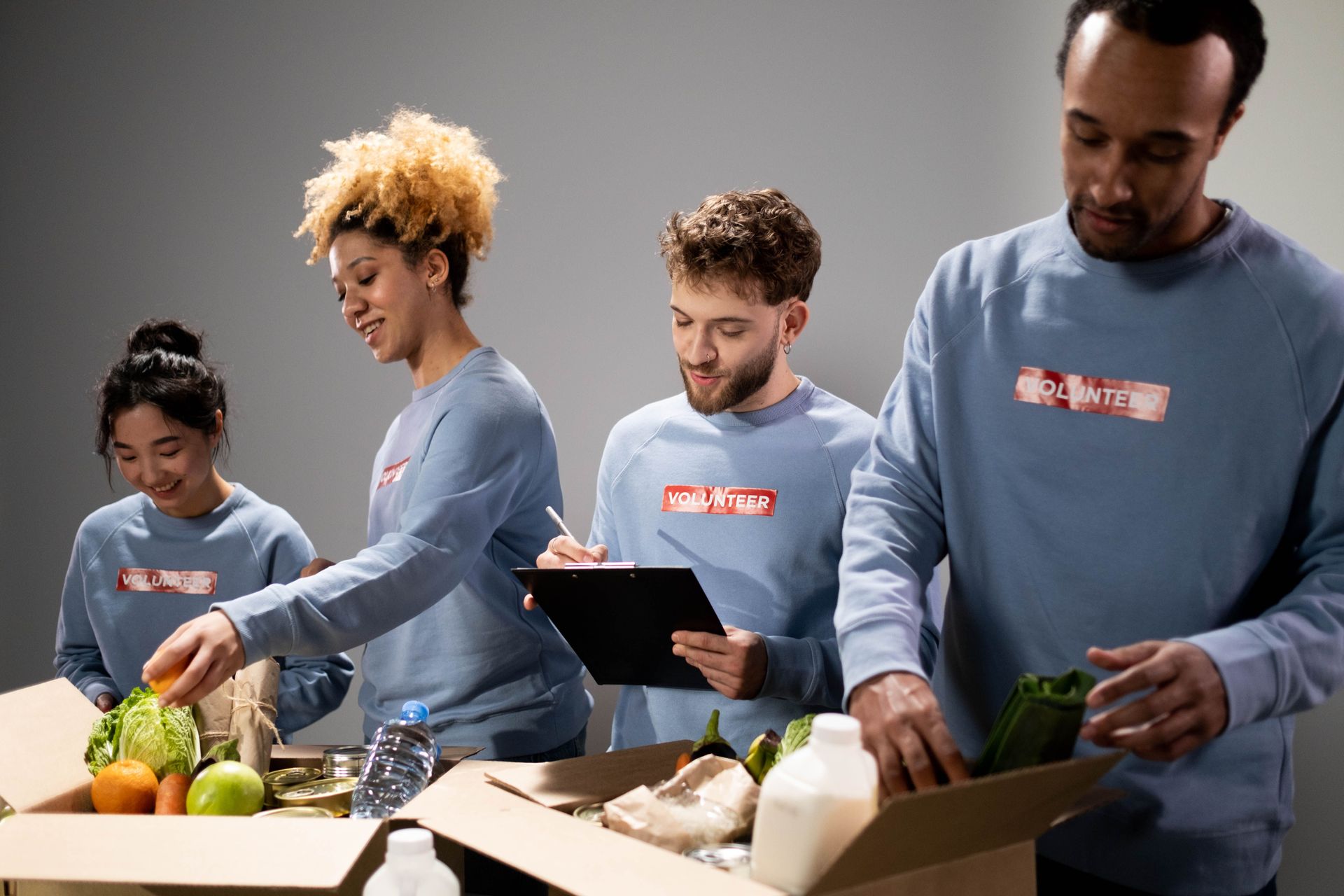 People packing produce and groceries at a table, with one person using a tablet