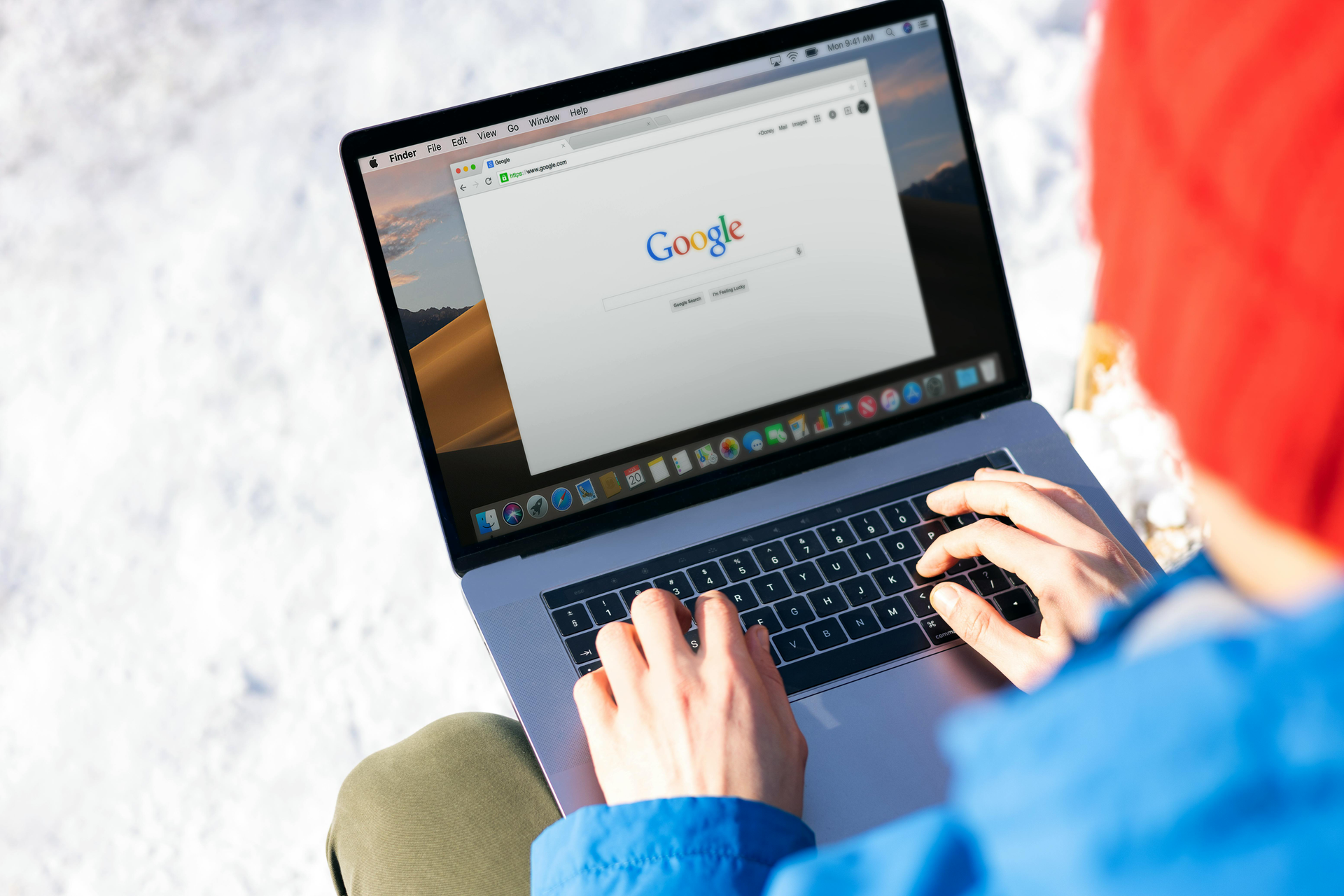 Person typing on a laptop outdoors, with Google open on the screen.
