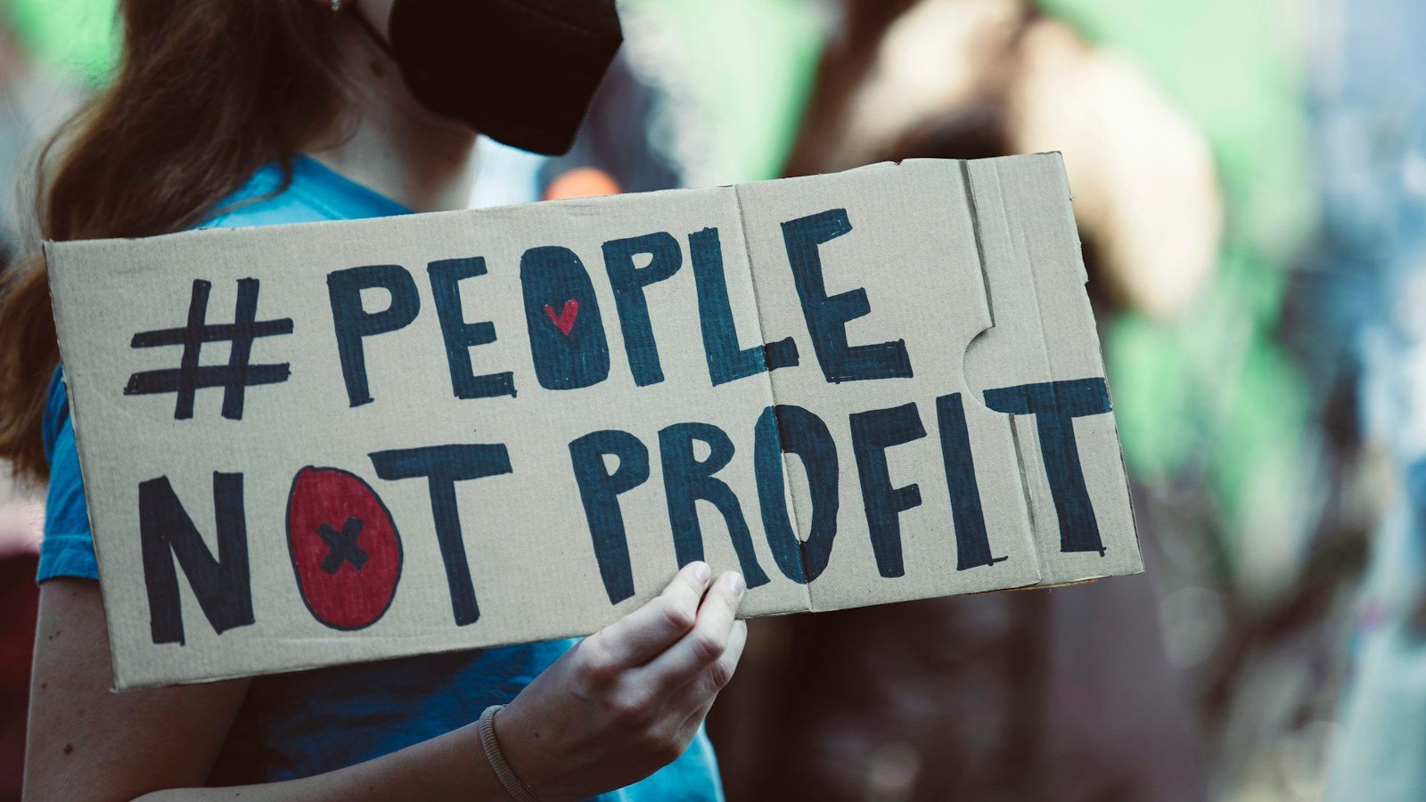 Person holding a sign reading “#PEOPLE NOT PROFIT” at a protest