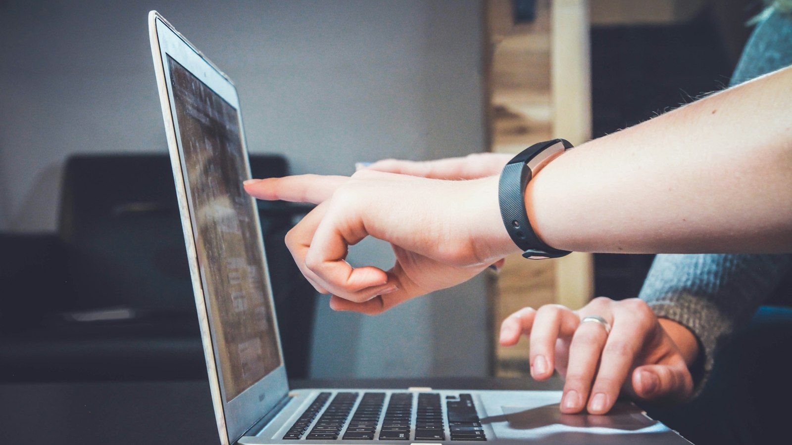 Person pointing at a laptop screen while another types on the keyboard