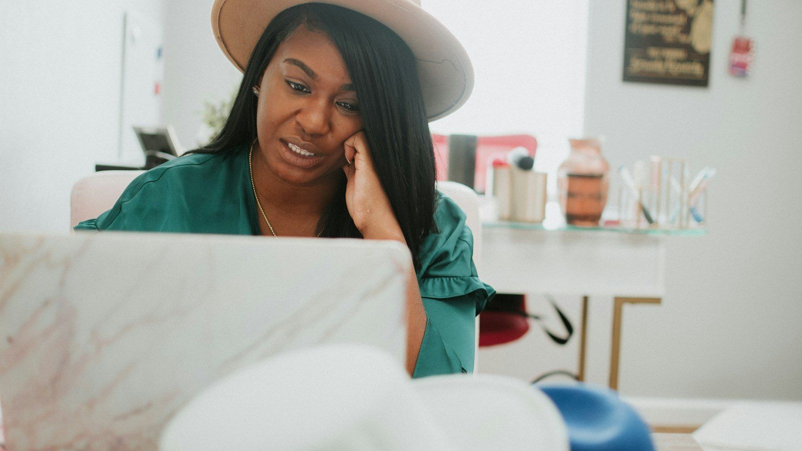 Smiling woman in a hat, using a laptop at a desk in a bright room