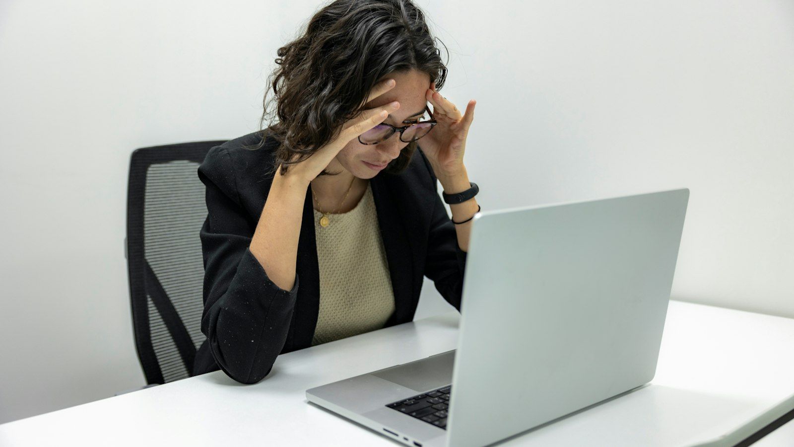 Person at a desk rubbing eyes while looking at a laptop, appearing tired or stressed