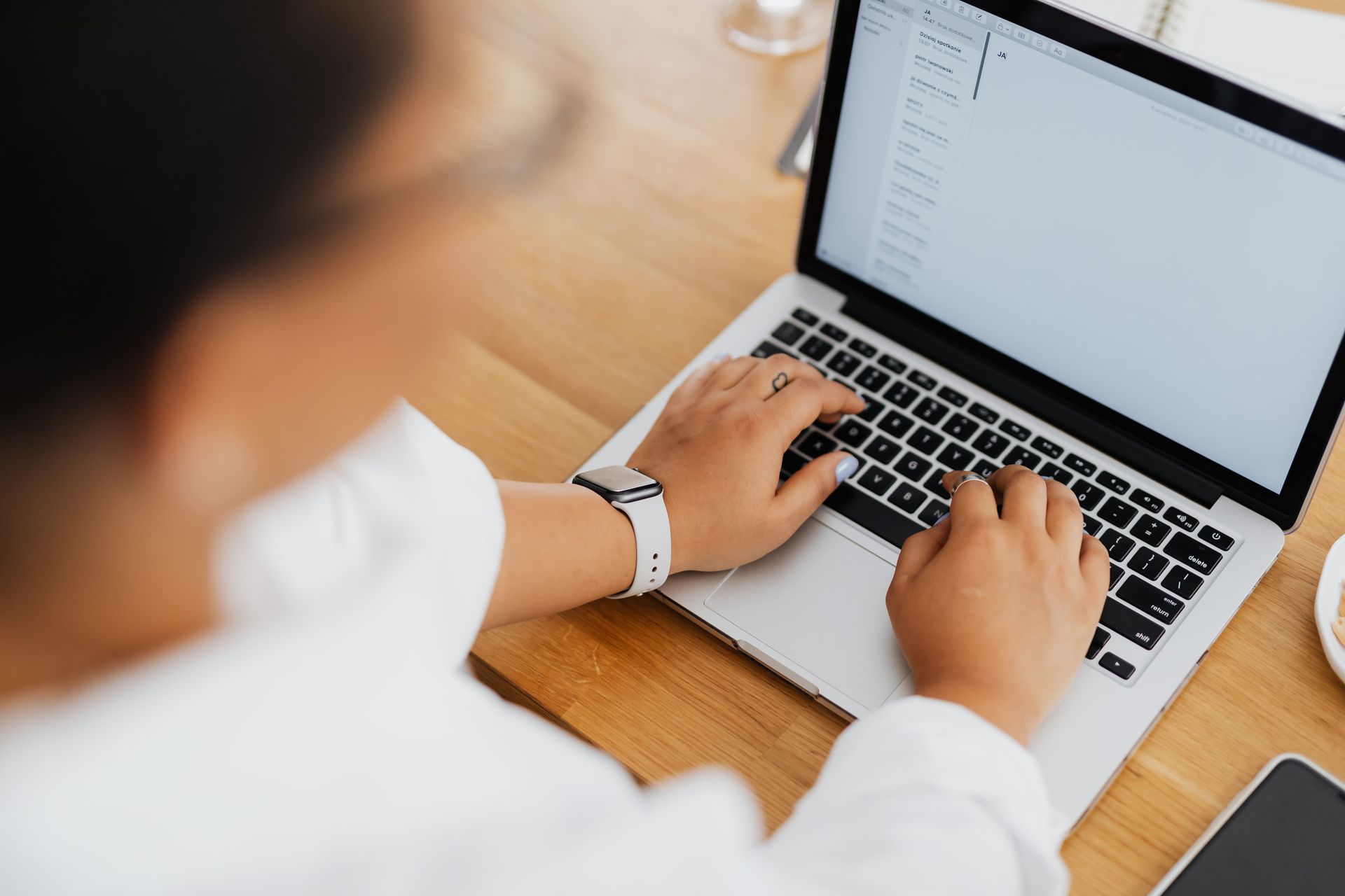 Person typing on a laptop at a wooden desk with a smartphone nearby
