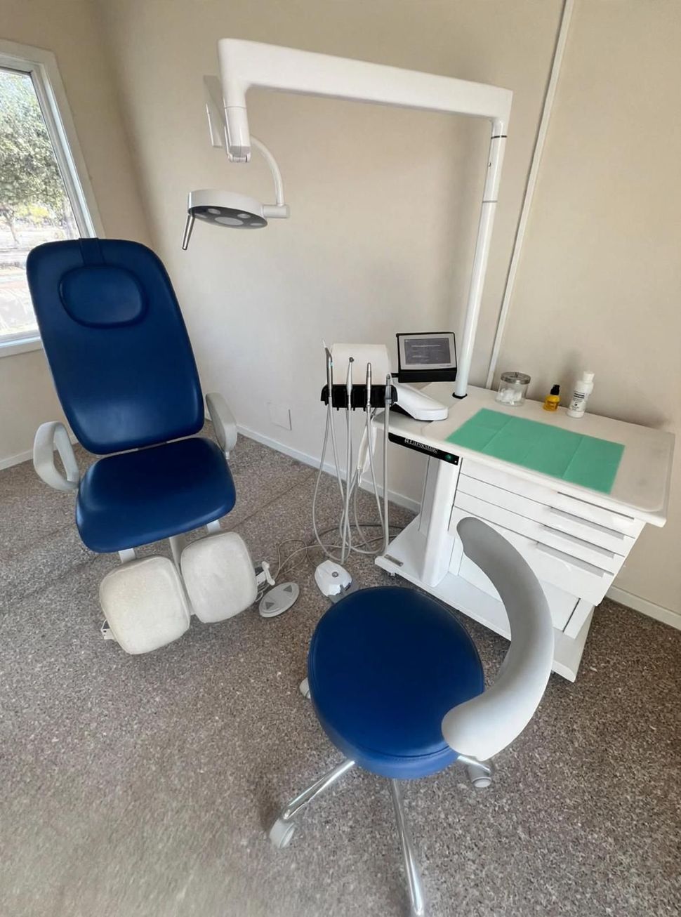 Sala per visite odontoiatriche con poltrona reclinabile, lampada scialitica, armadietti e un piccolo carrello portastrumenti