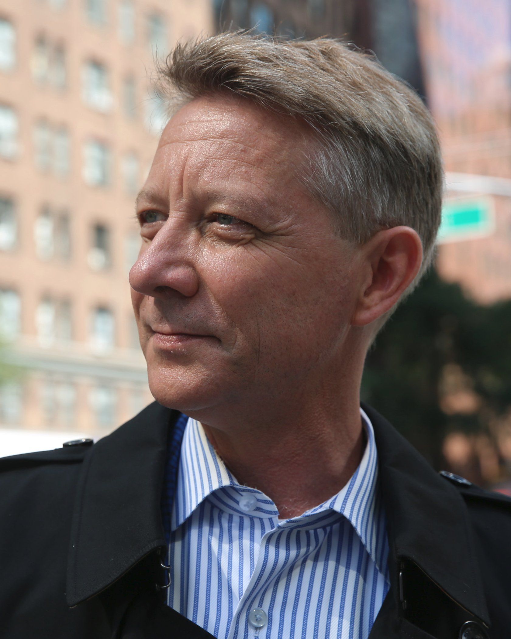 Man looking left outdoors with blurred city buildings behind him
