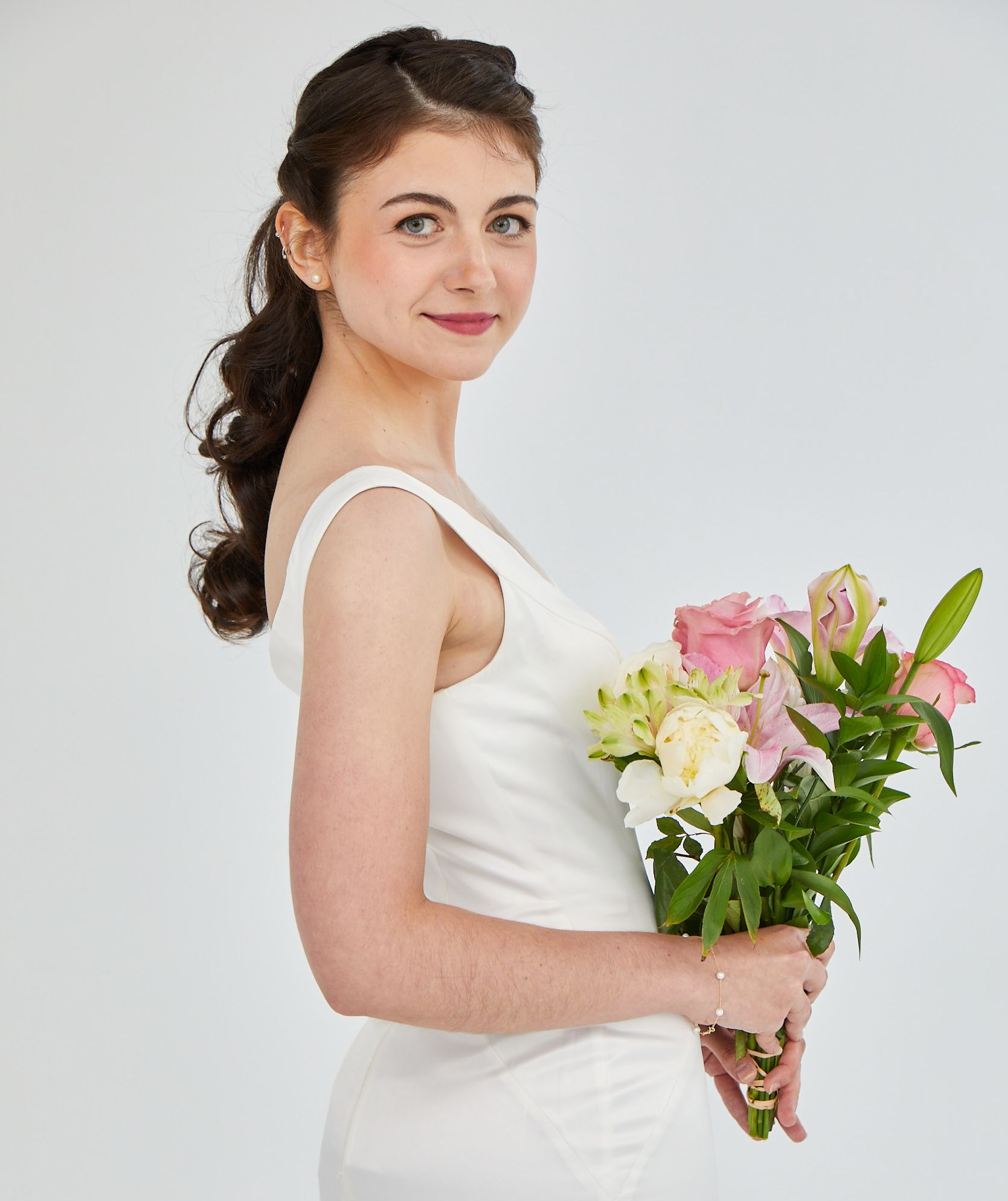 Woman in a white dress holding a bouquet of pink and white flowers against a light background