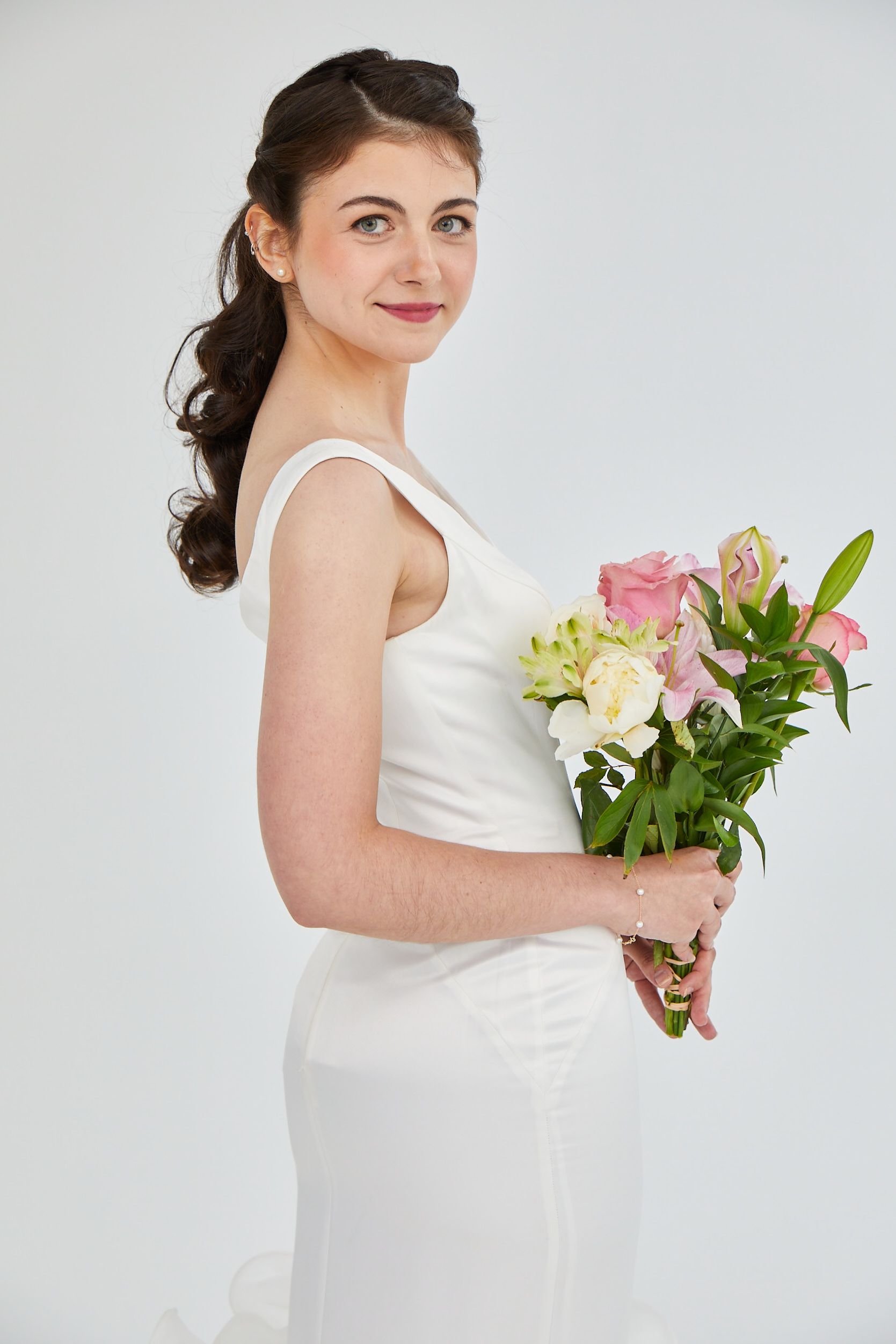 Woman in a white dress holding a bouquet of pink and white flowers against a light background