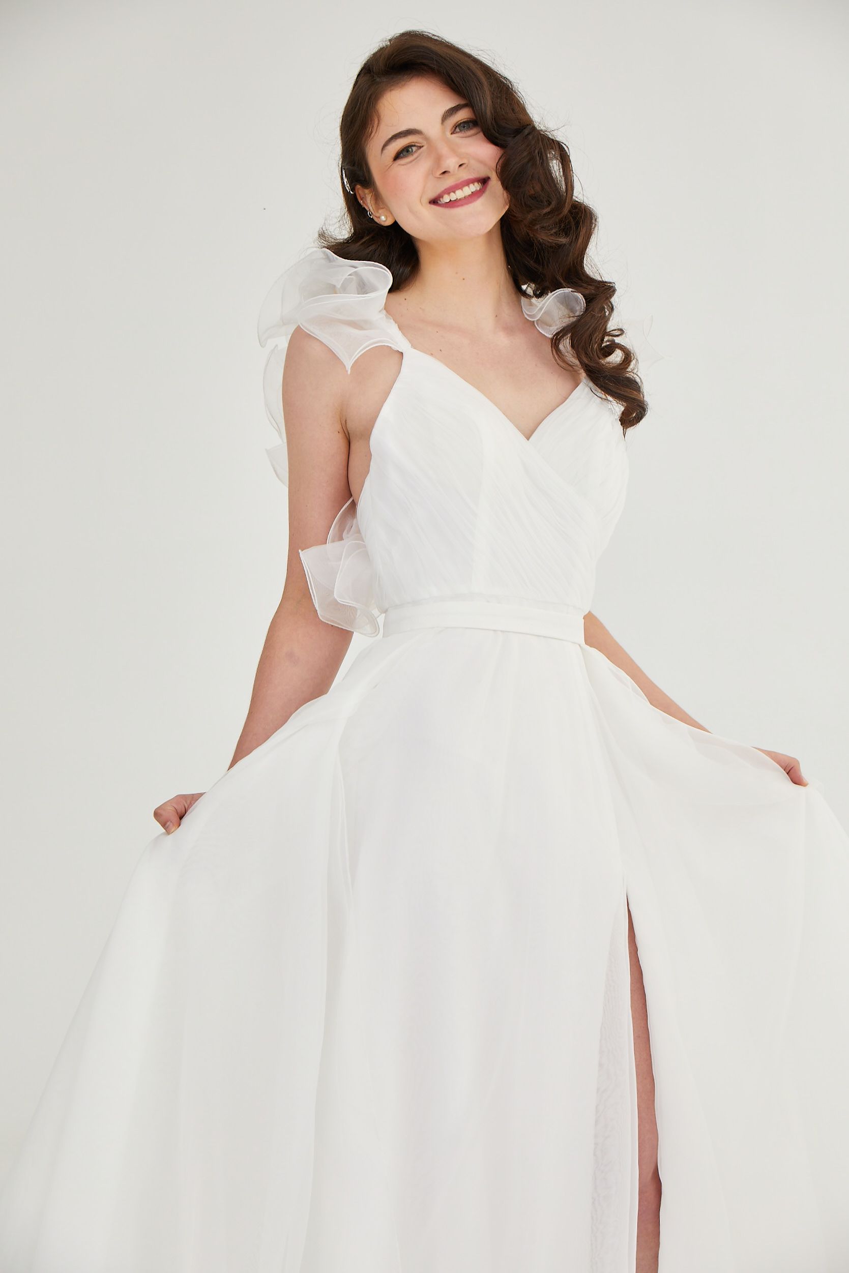 Woman in a white dress smiling and holding the skirt against a plain light background