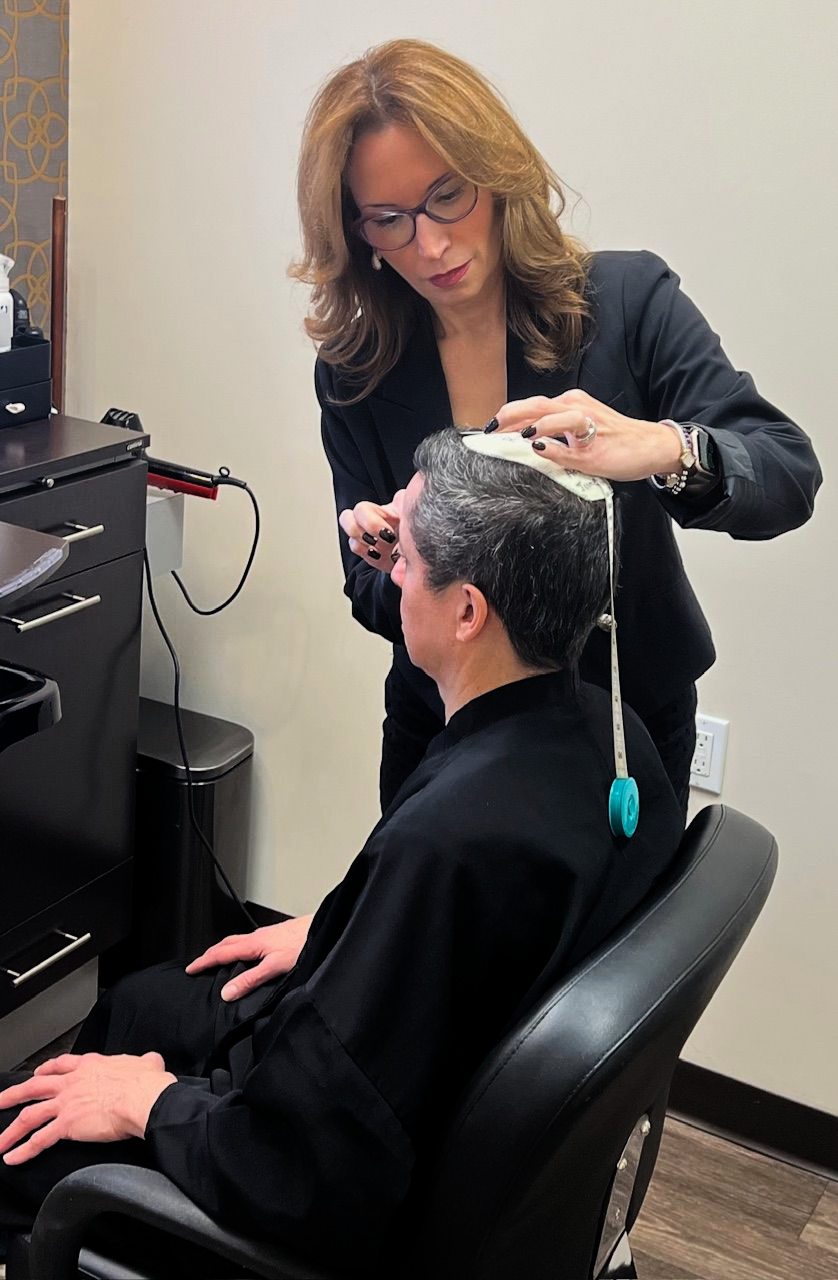 Stylist measures a seated client’s scalp in a salon, while holding a mold on the client's head.
