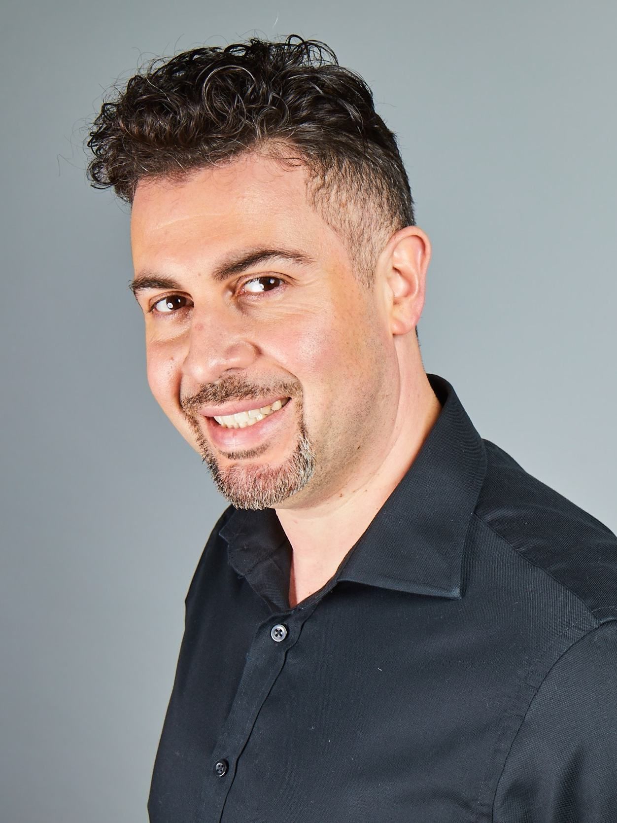 Smiling man in a black shirt against a light gray background