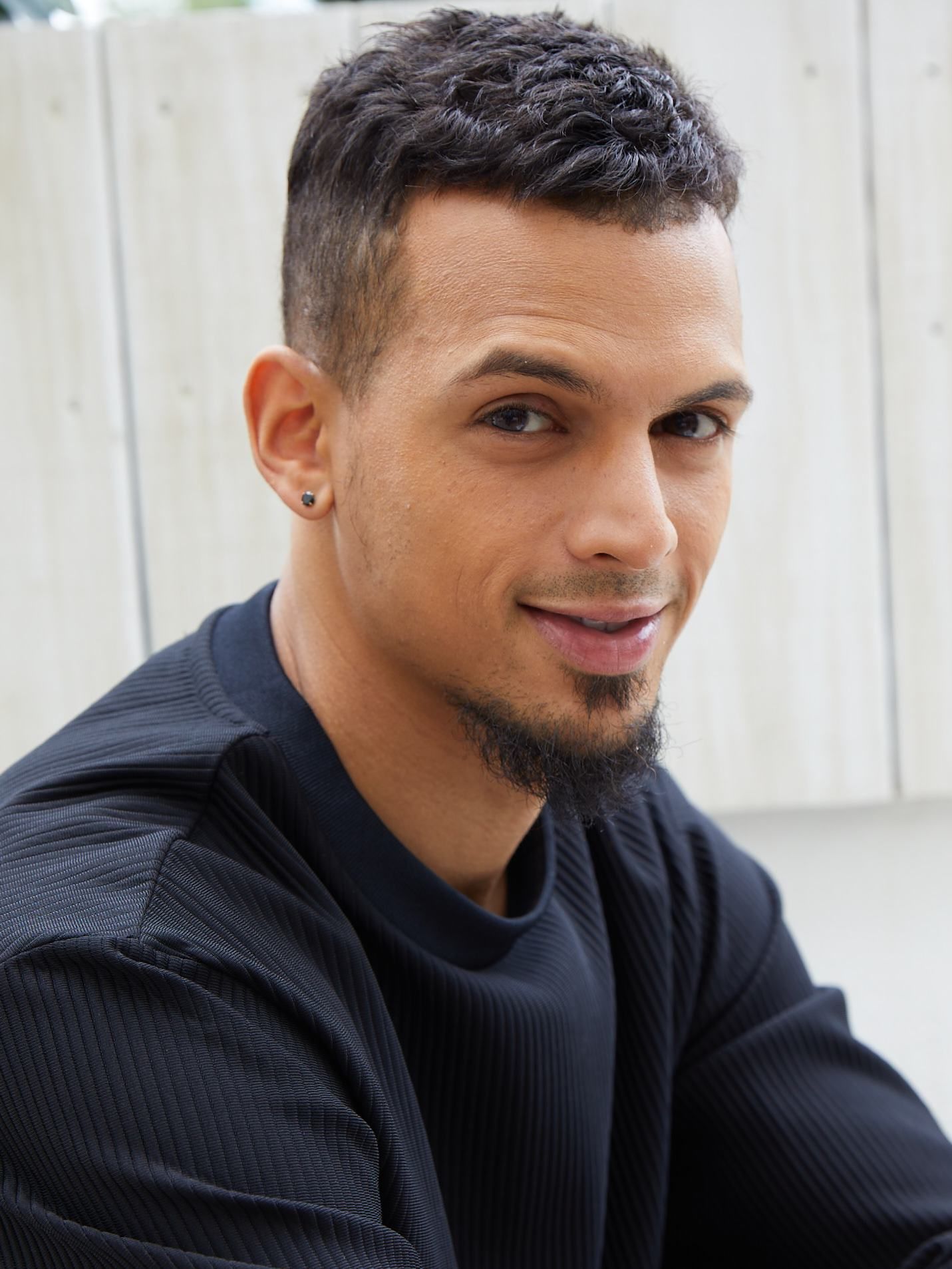 Portrait of a smiling man in a black sweater, seated indoors against a bright window background