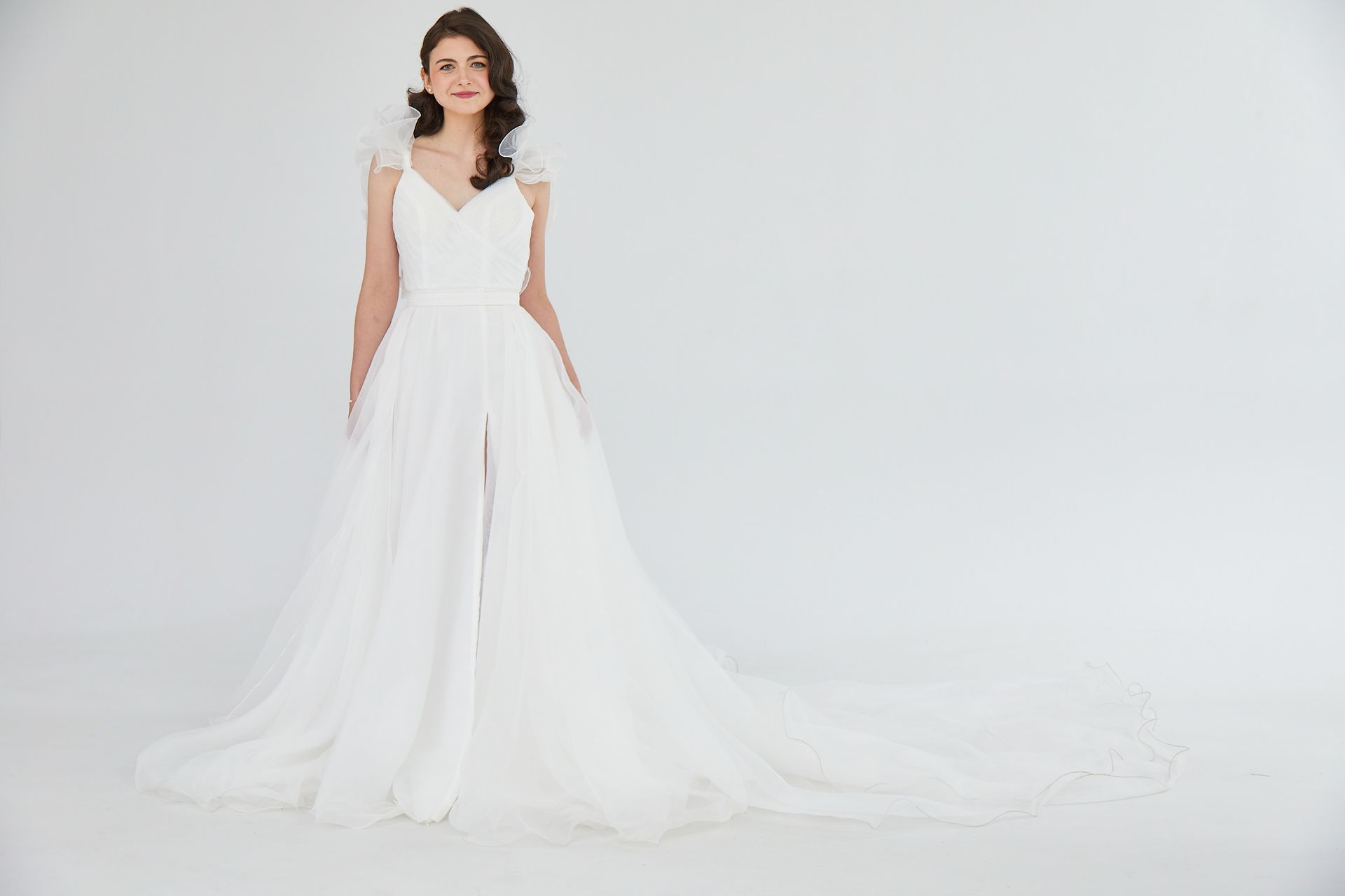 Woman in a flowing white wedding dress standing against a white studio backdrop