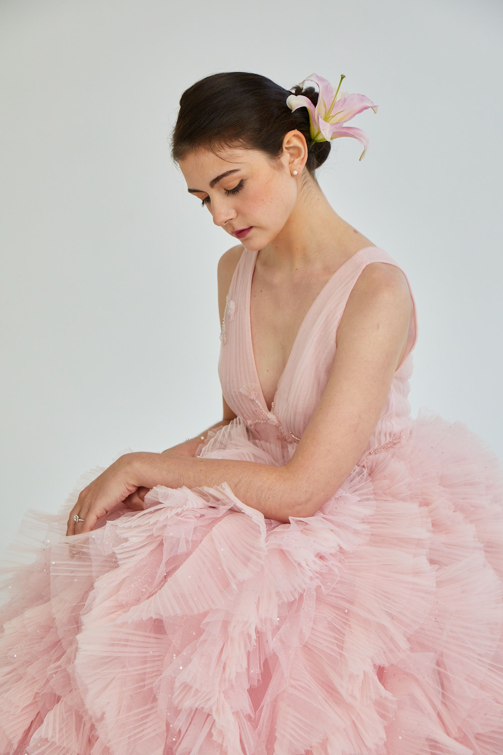 Woman in a pink tulle dress seated in profile against a light gray background