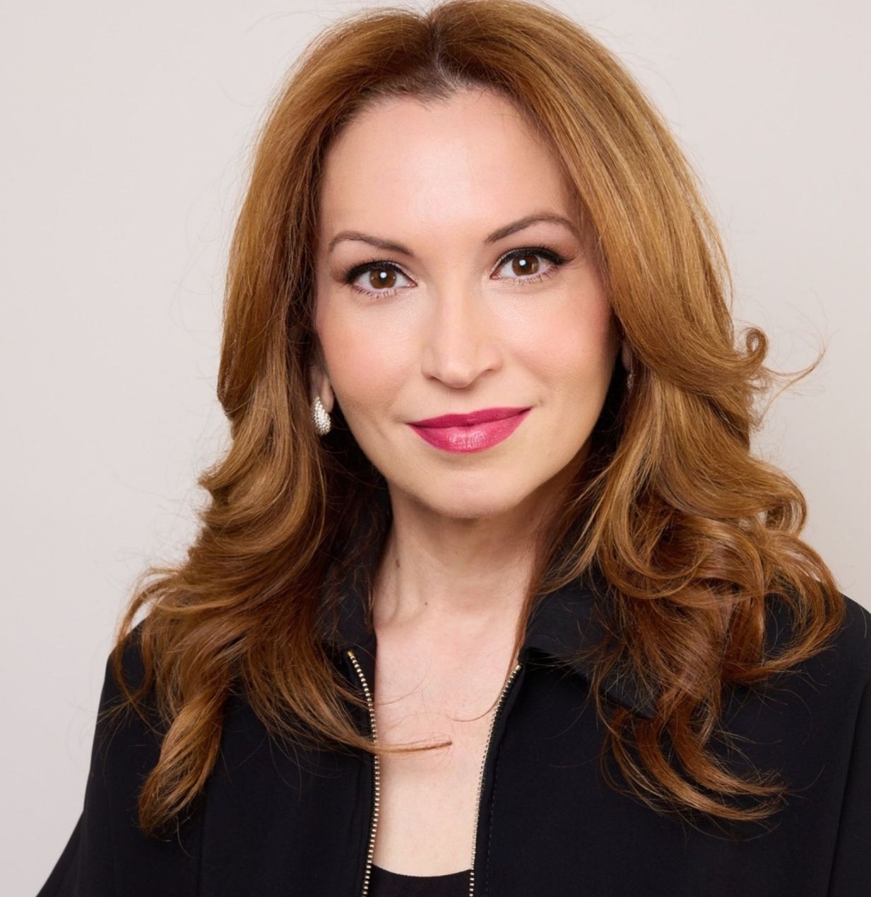 Headshot of a woman with auburn hair in a black blazer, smiling against a light background