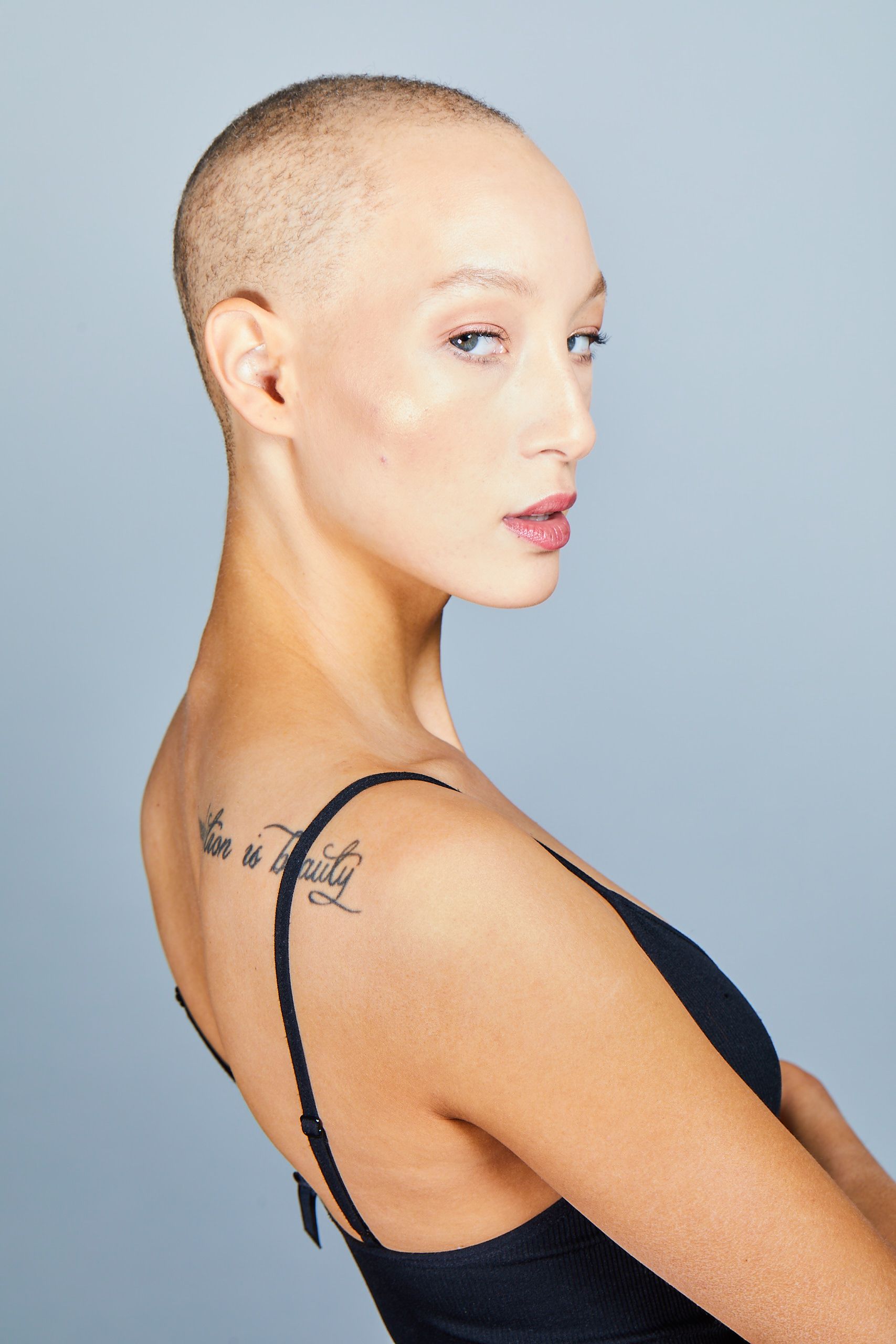 Side-profile portrait of a person with a shaved head wearing a black top against a light gray background