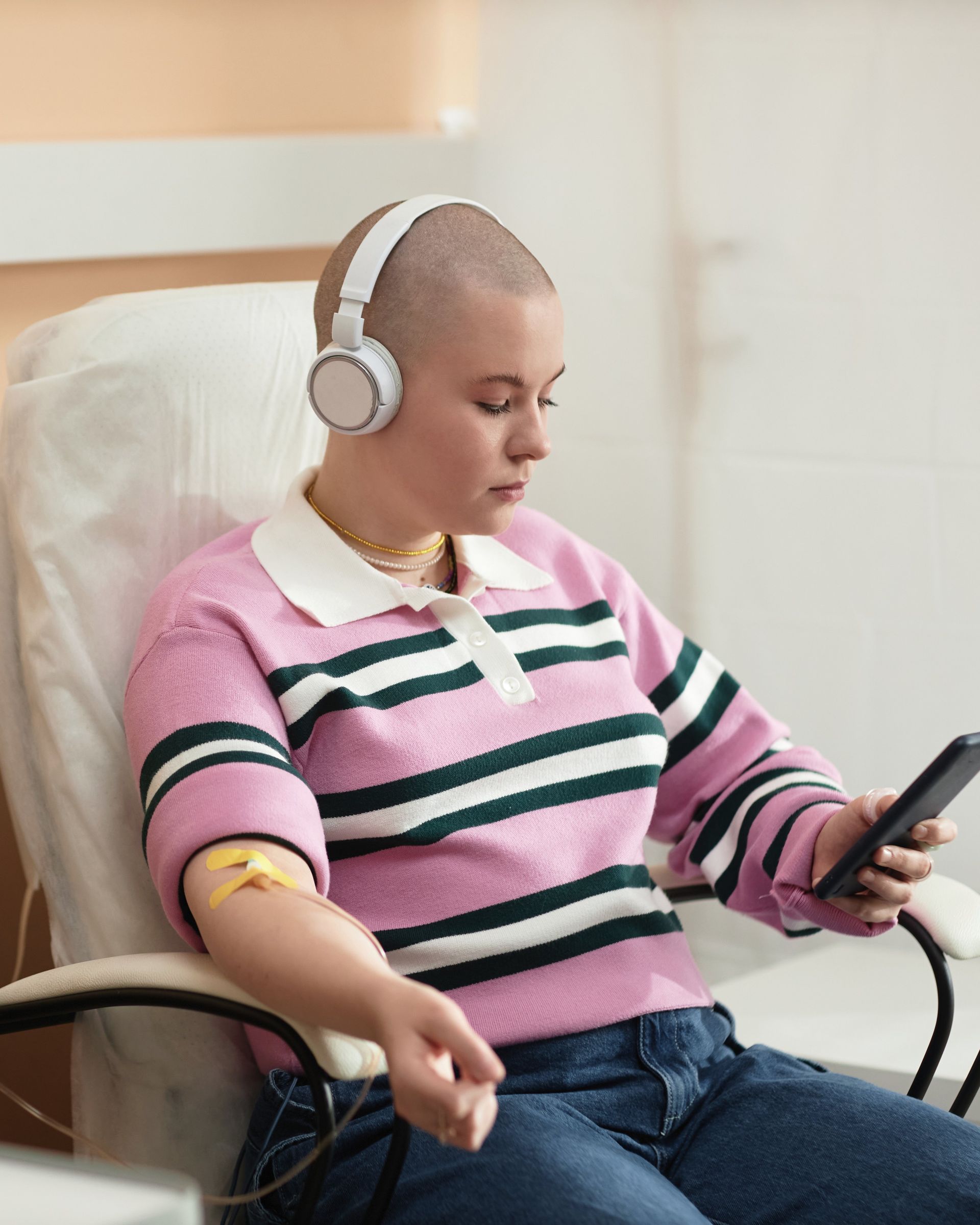 Person wearing headphones and a pink striped sweater using a smartphone while seated in a chair