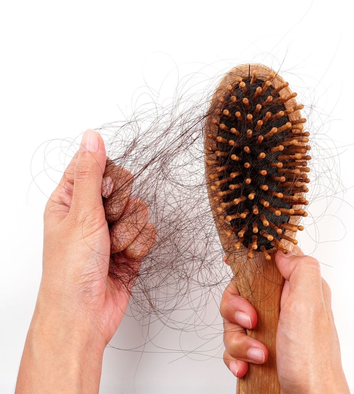 Hands brushing tangled hair from a round bristle brush over a white background