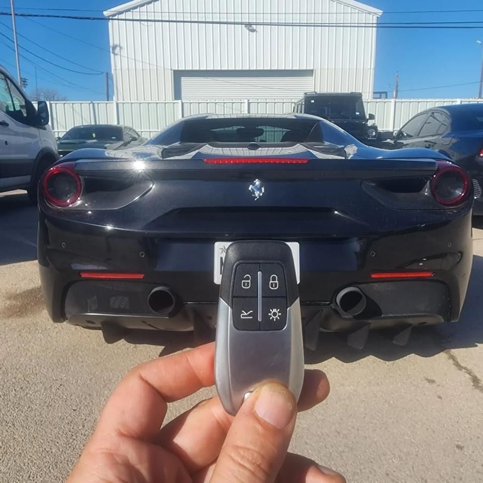 Hand holding car key fob in front of a black Ferrari.