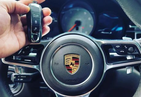 Hand holding a car key over the steering wheel of a Porsche.