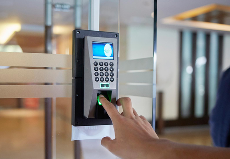 Finger pressed on a biometric scanner on a glass door for access control.